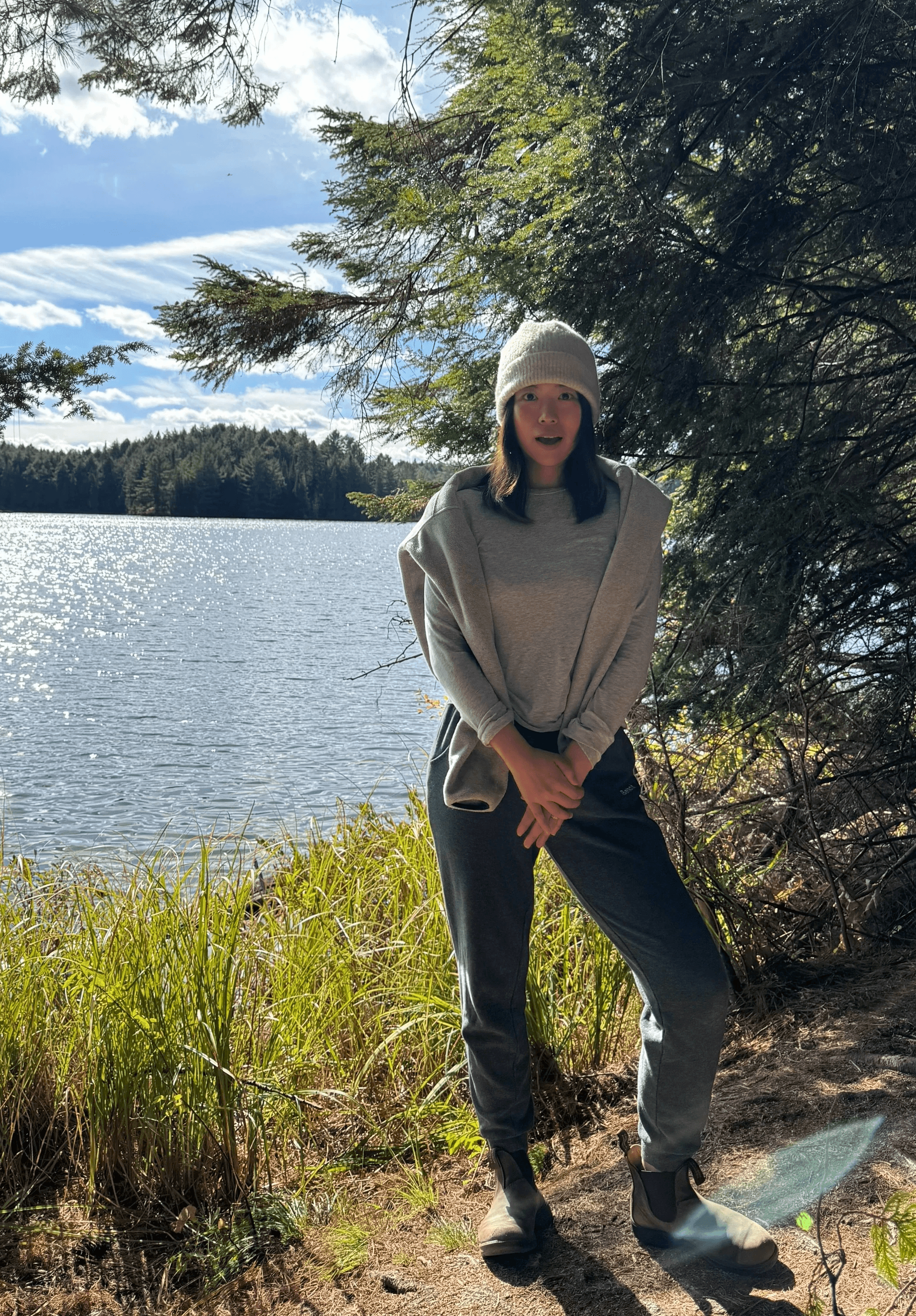 Person wearing a blue puffer jacket and red backpack standing in front of a light blue building on a city street.