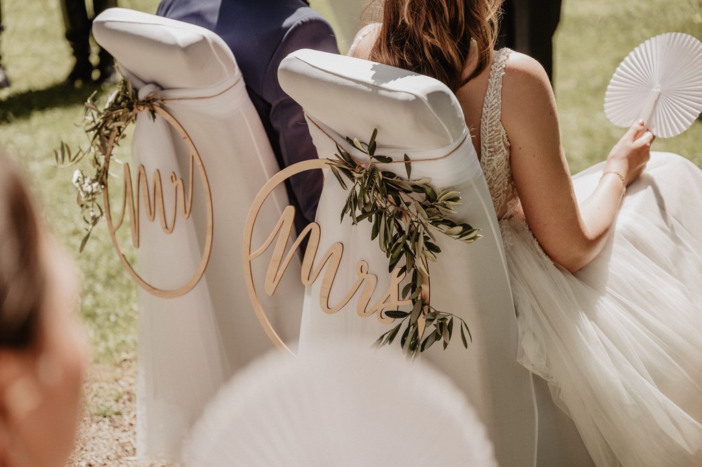 Die dekorierten Stühle des Brautpaares bei einer freien Trauung im Freien – Mr. & Mrs. Holzschilder mit Olivenzweigen auf Marrymind entdecken.