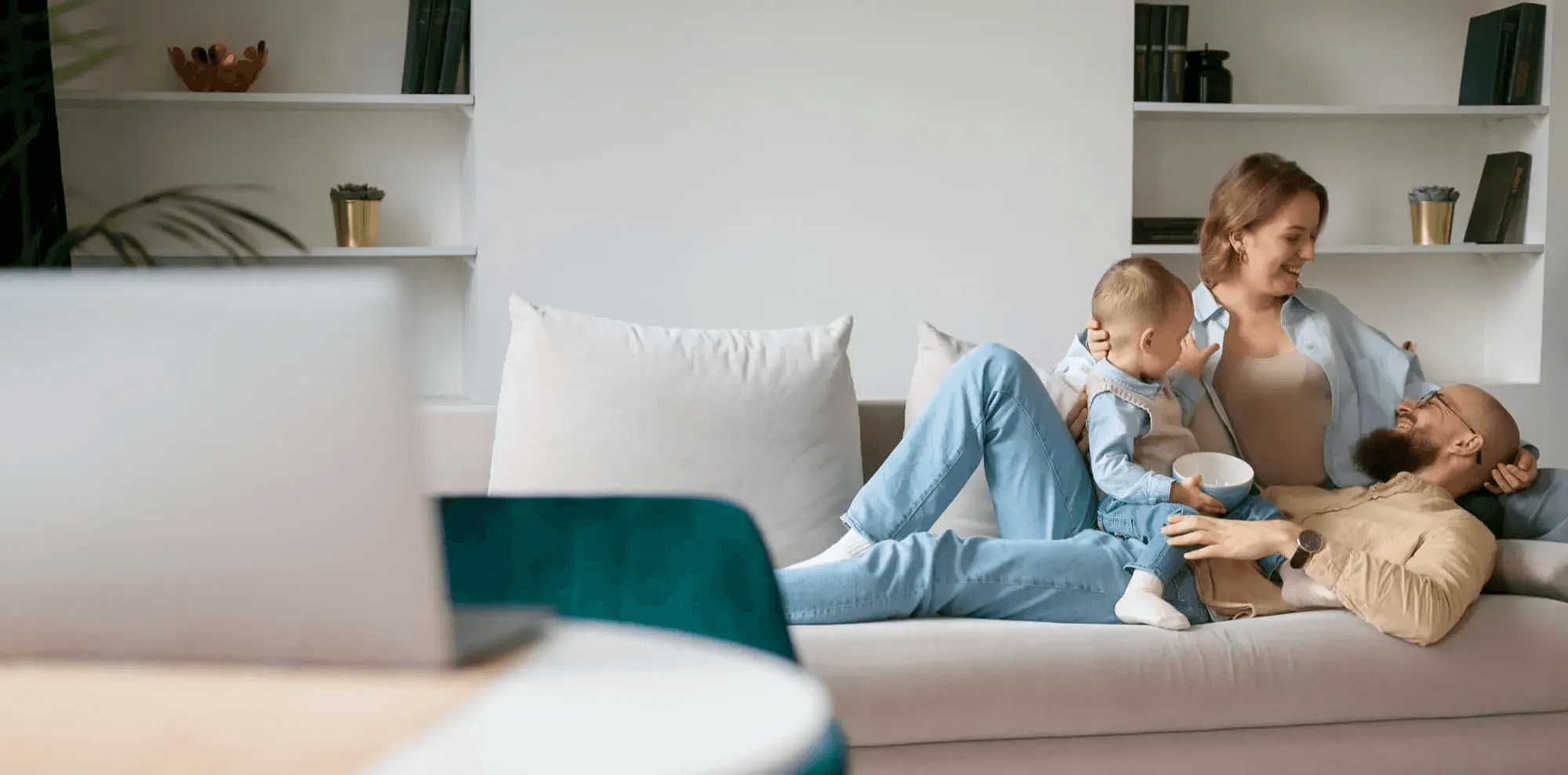 A young family relaxes together on a cozy couch in their modern living room, smiling and enjoying time with their baby. The warm, inviting setting reflects the comfort and stability made possible through FHA home loans from Chris Lewis Home Loans.