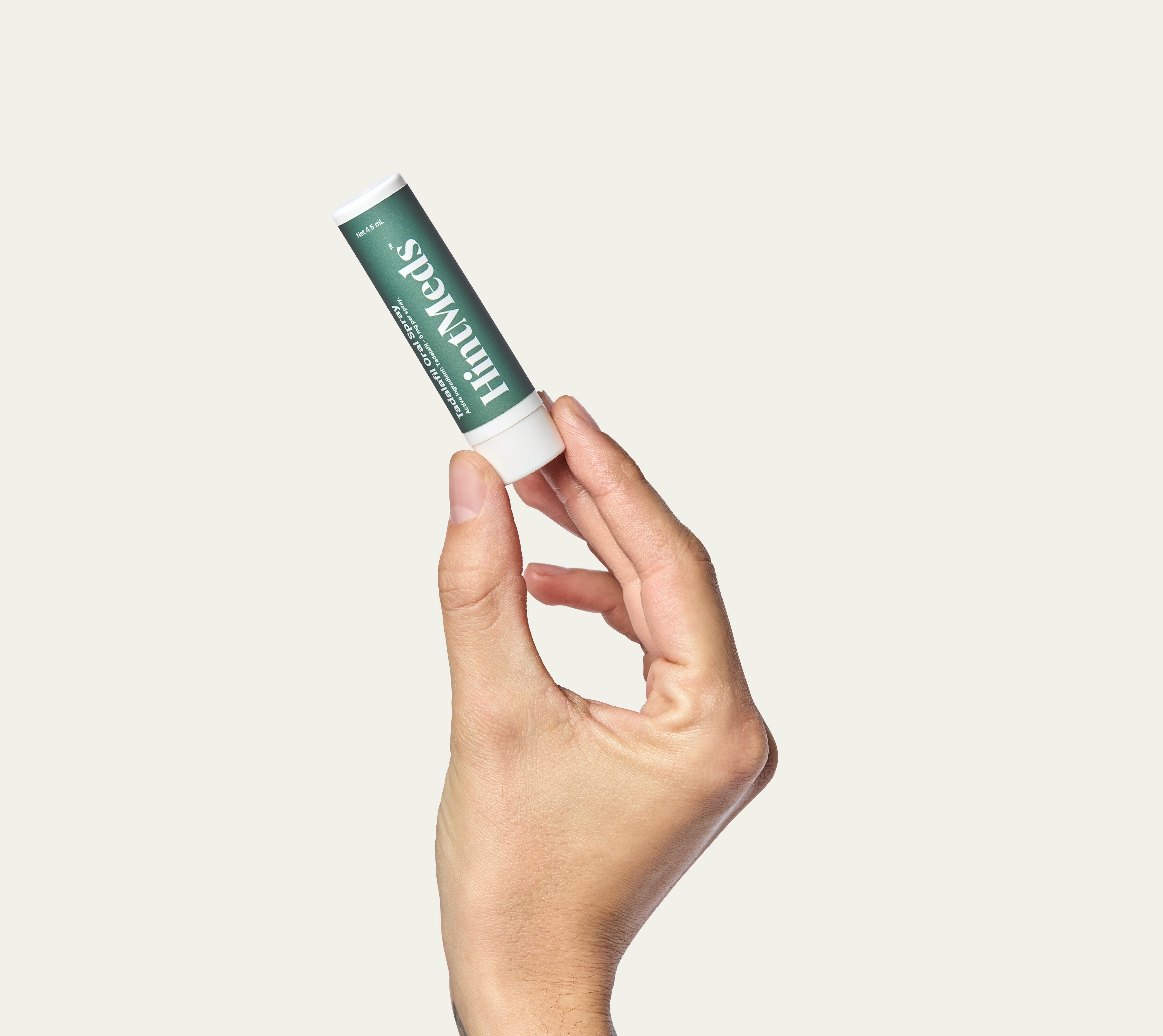 A hand holds a small tube of product against a light background.