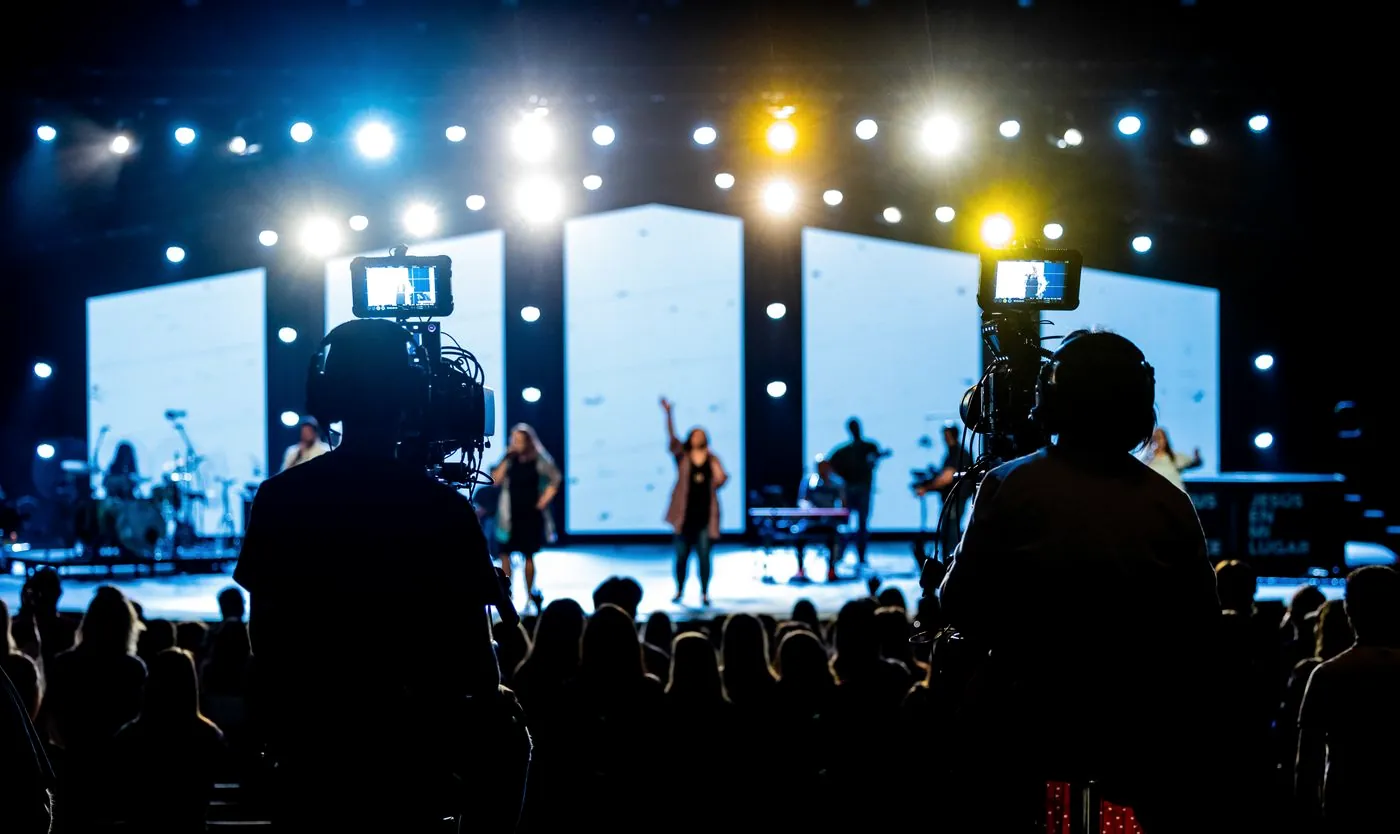 Camera operator filming the worship band from the back of the room