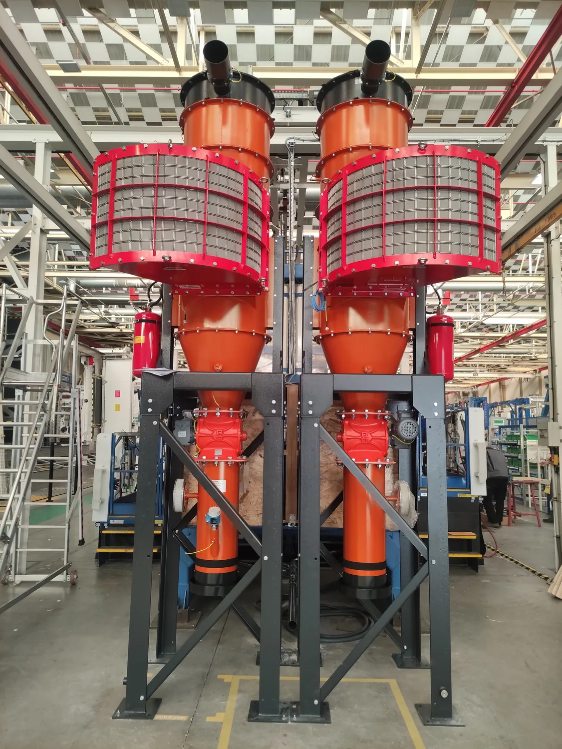 Deux cyclones d’aspiration industrielle orange, équipés de protections grillagées et installés sur une structure métallique.