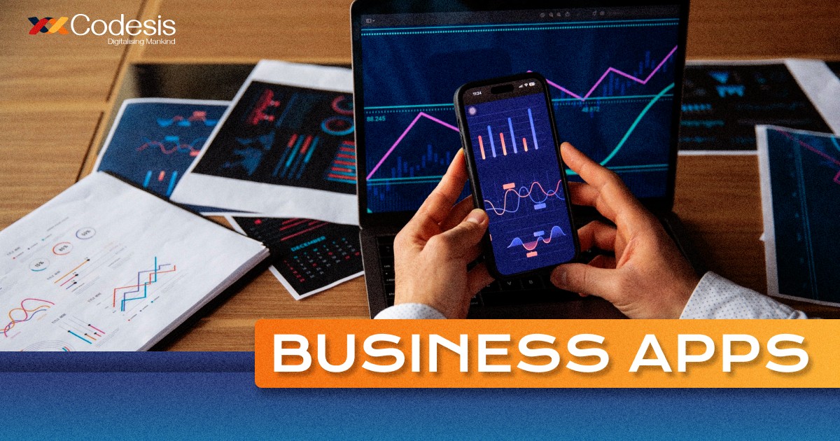 an image of a person using business apps on mobile phone and a laptop kept on the desk showing trading graph also some books and papers on the table showing trading graphs and trading analytics