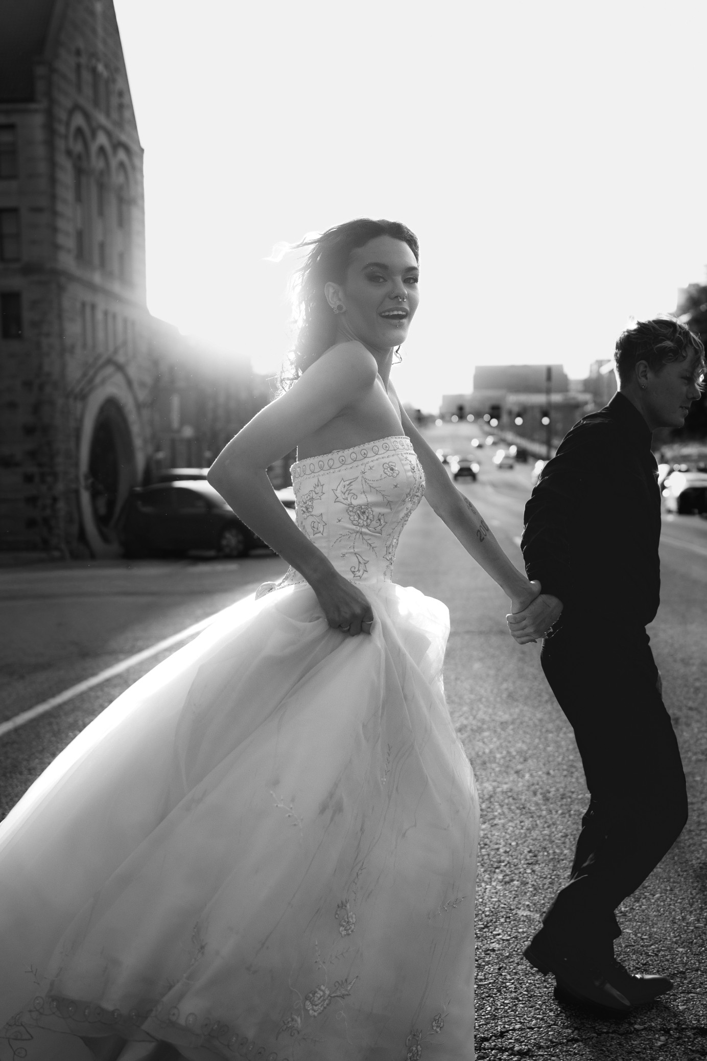A couple in wedding attire walks hand in hand across a sunlit field.