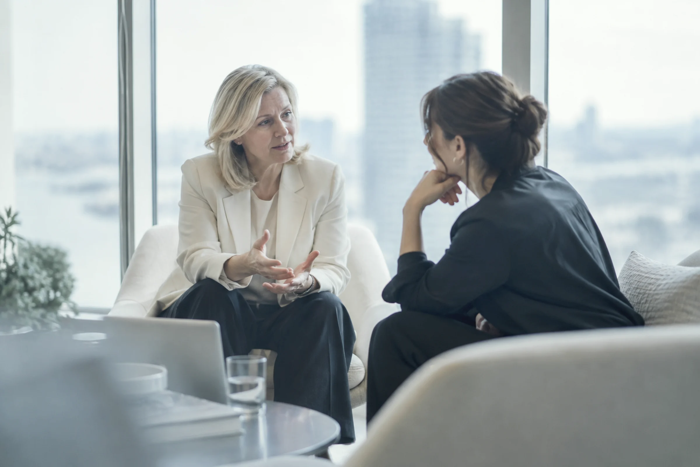 A people leader in conversation with a colleague in lounge chairs by a window