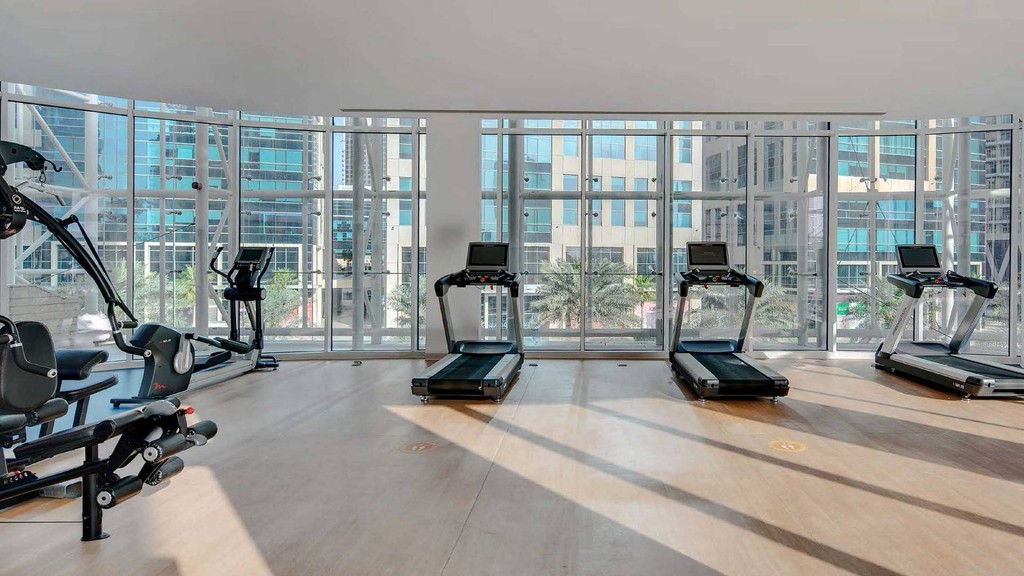  A gym room at The Pad by OMNIYAT featuring a large window and a spacious mirror reflecting the workout space.