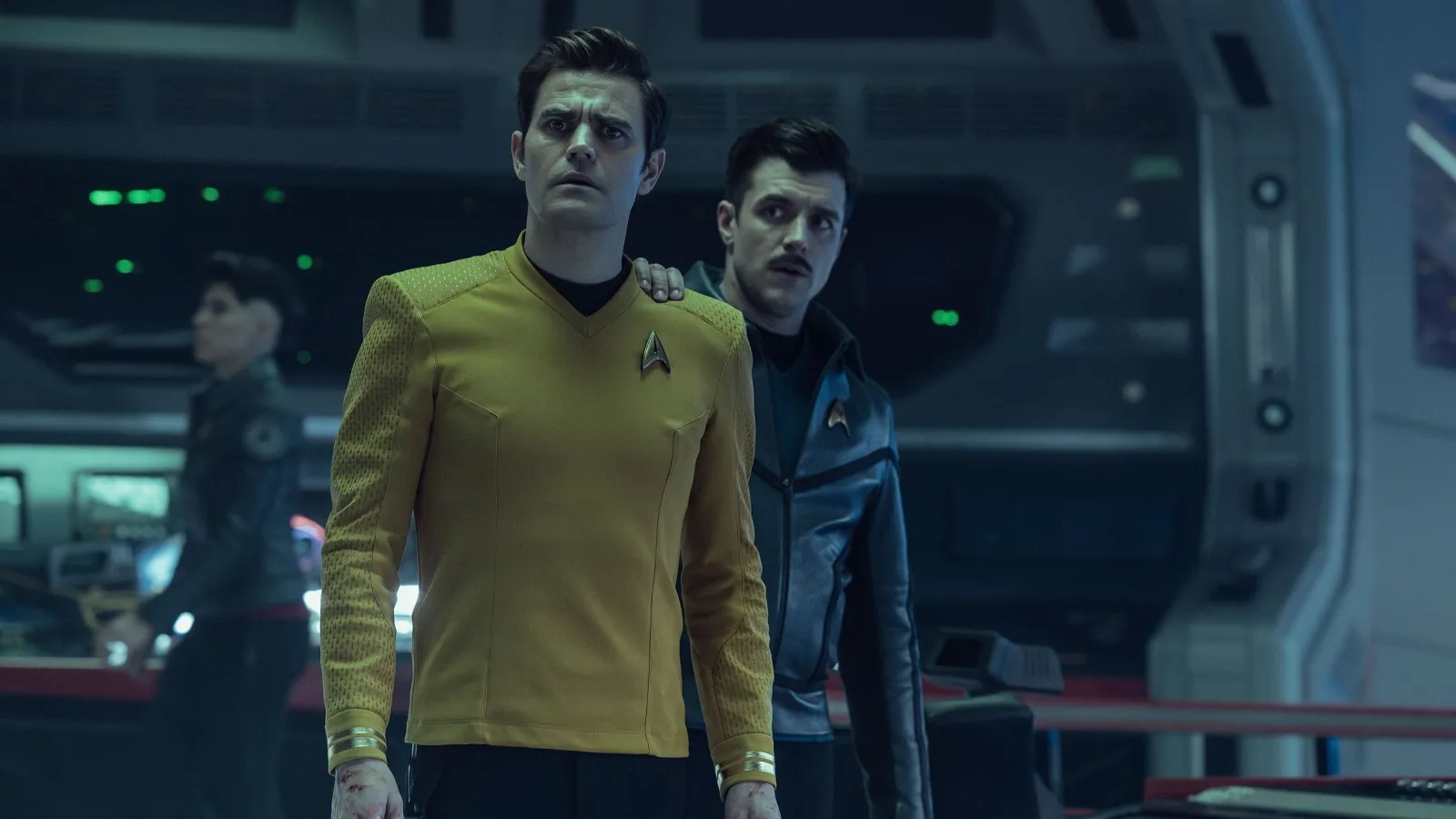 Two individuals in Starfleet uniforms are standing on a futuristic spaceship's bridge, with one placing a reassuring hand on the other's shoulder, surrounded by advanced technology and control panels.