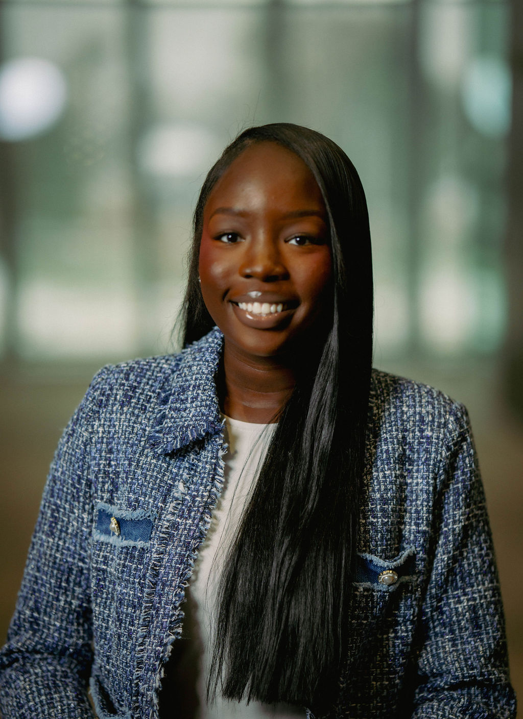 A person in a brown suit and cream scarf poses against a neutral background, showcasing elegant and classic fashion.