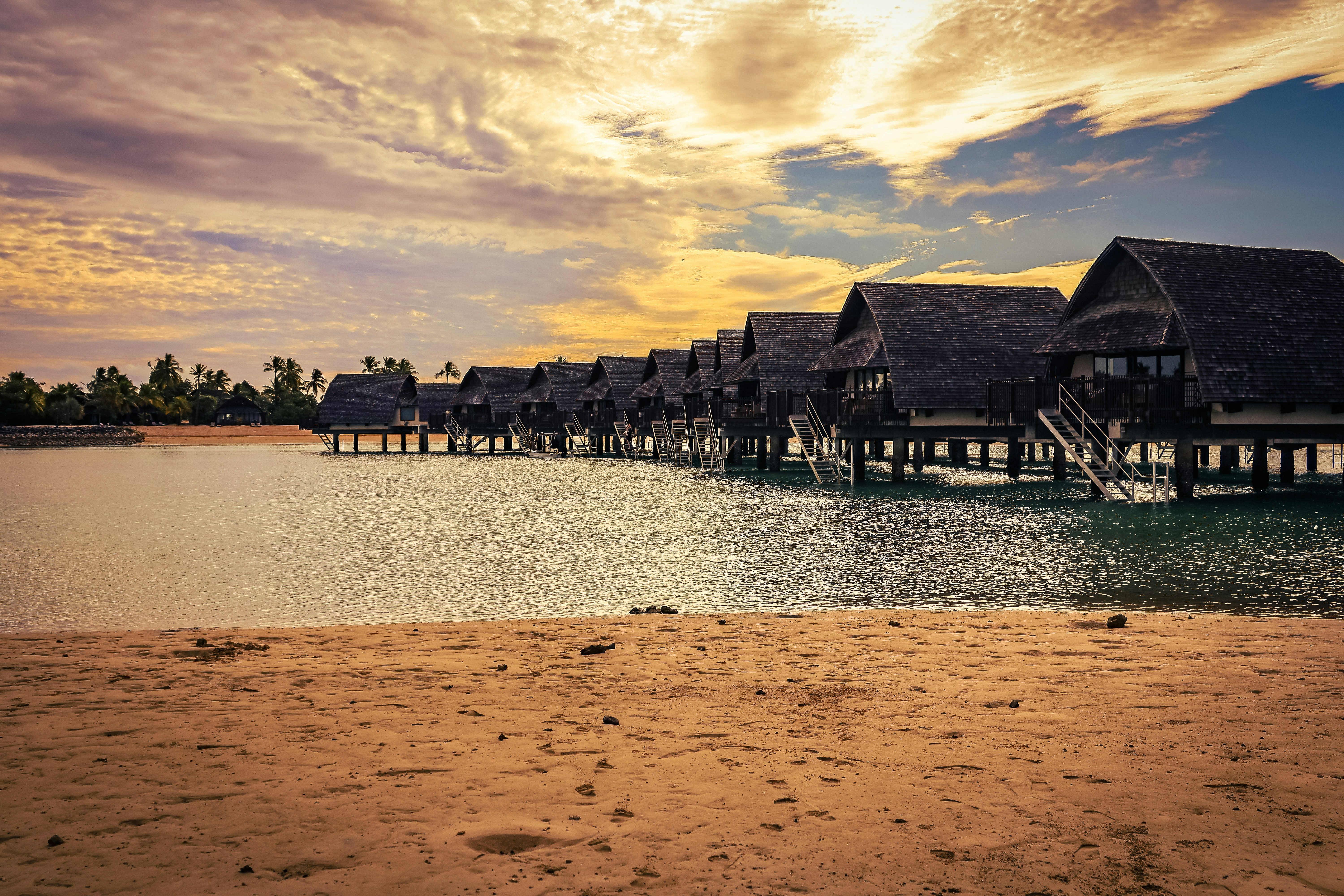 Overwater bungalows line a calm sea at sunset.