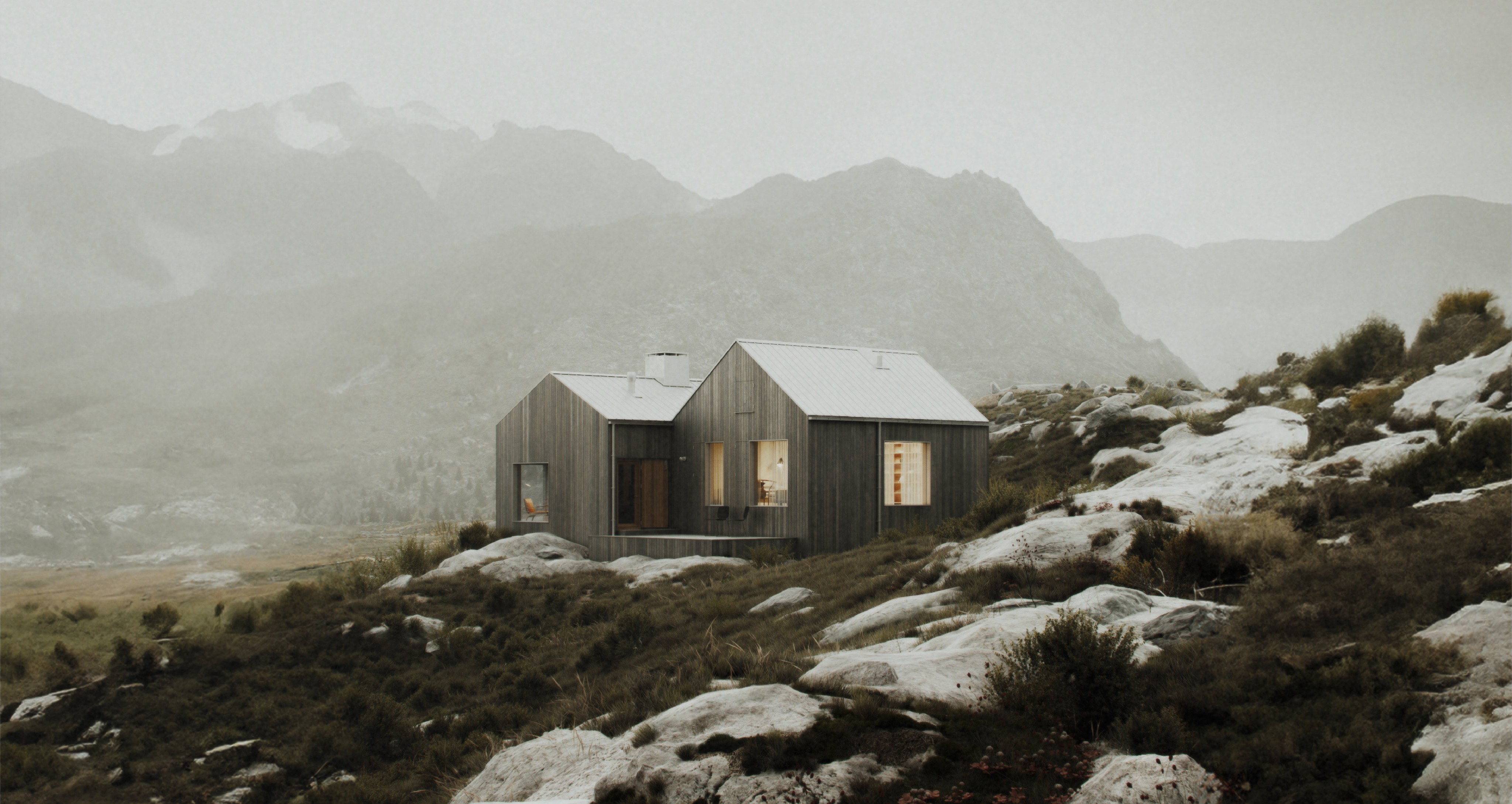 Wooden cabin with warm-lit windows and a metal roof, sitting on a rocky, grassy slope in a misty mountain valley
