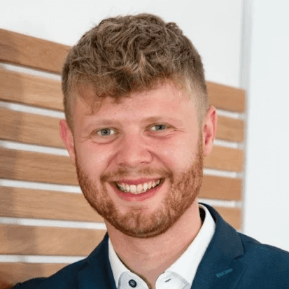 Rupert Zeltsperger steht im Anzug vor einer Wand und lächelt