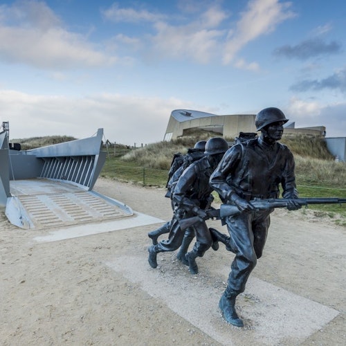 复制的登陆艇上，穿着战斗装备的士兵雕像正在奔跑，背景是一座博物馆建筑。