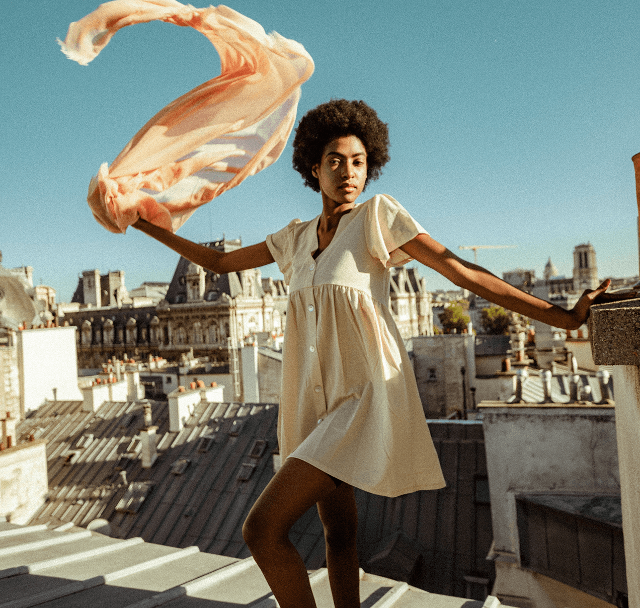 Woman in dress on Paris rooftop with scarf blowing in the wind