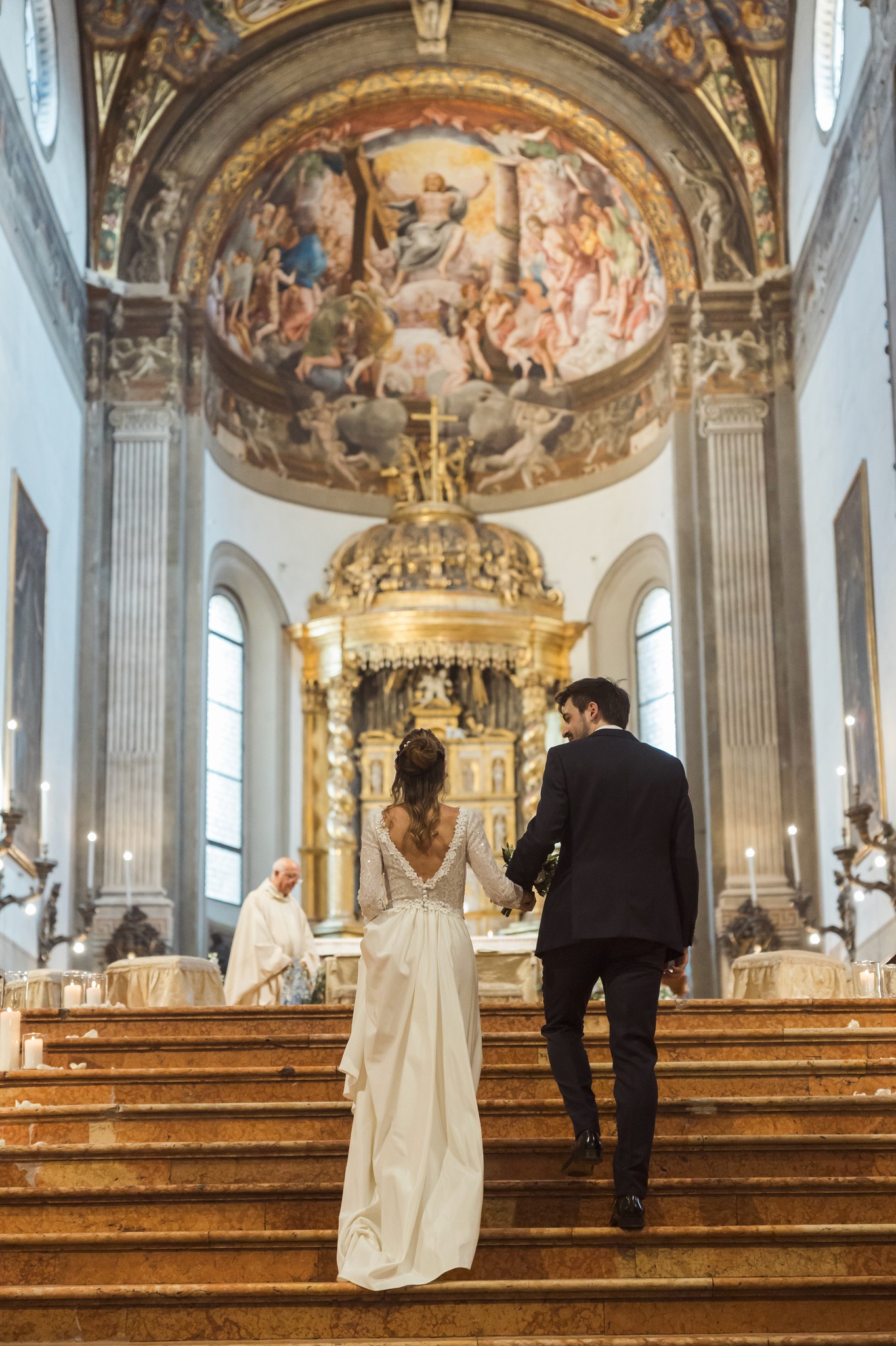 Sposi che salgono i gradini dell'altare in chiesa, lui in smoking nero, lei in abito bianco lungo, cerimonia matrimoniale
