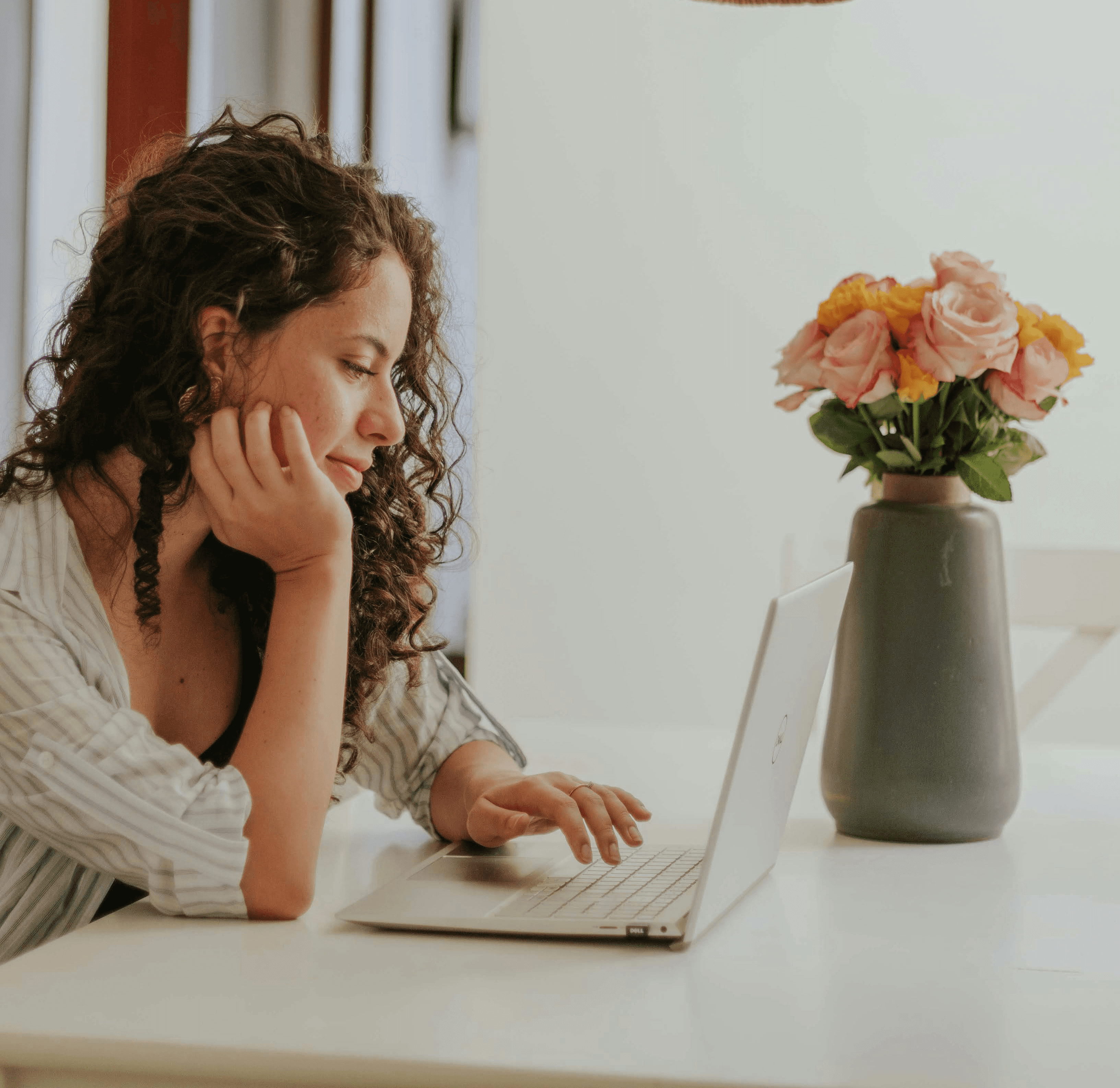 Donna che lavora al laptop da casa con un vaso di fiori accanto, rappresentazione del lavoro flessibile e dell’equilibrio tra vita privata e professionale.