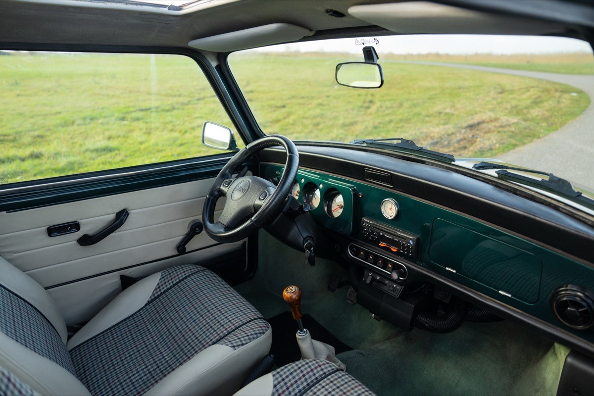 Interior view of a vintage vehicle showing the dashboard, steering wheel, and seats against an open field backdrop.