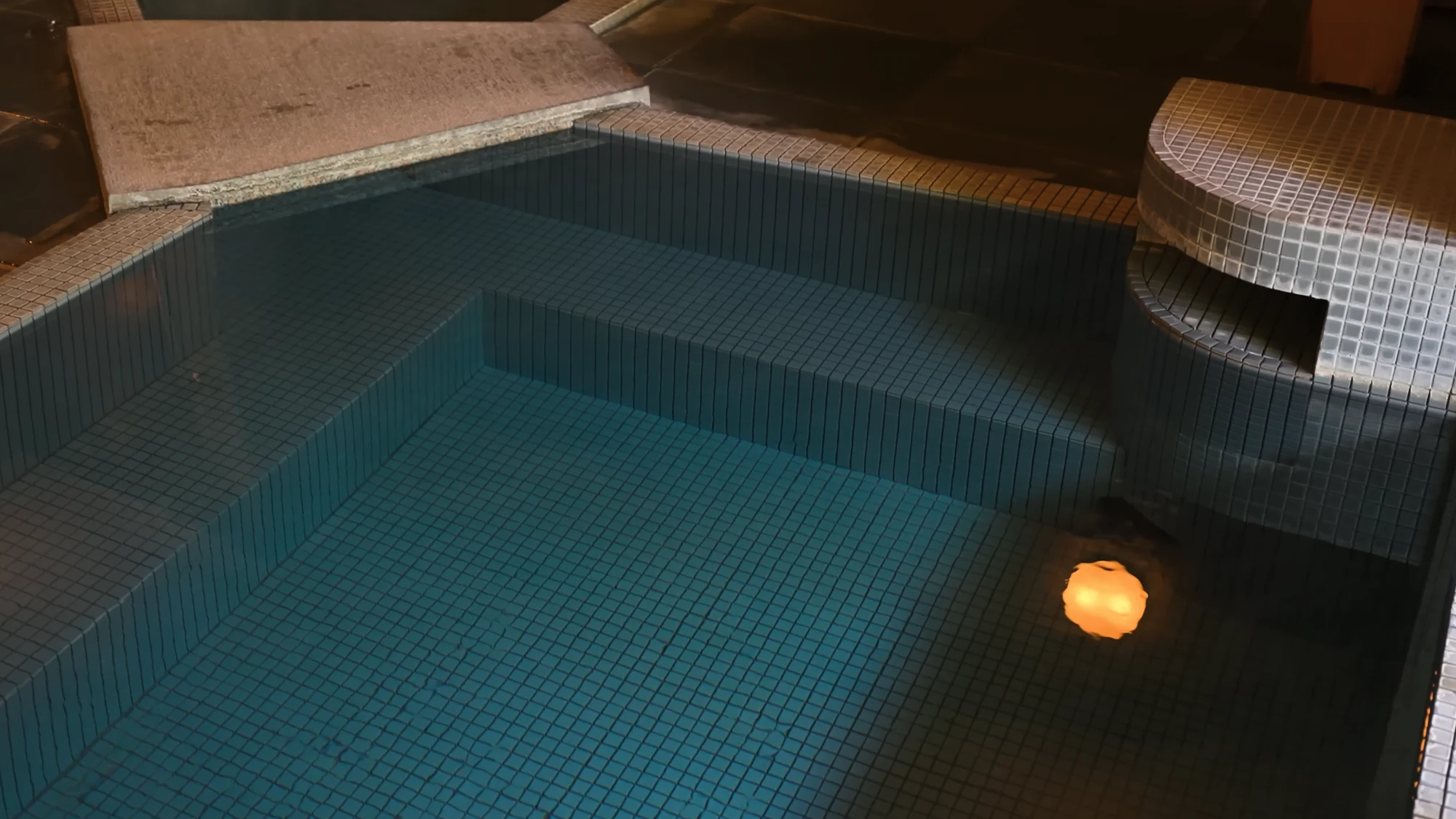 A large tiled indoor bath in Kinosaki lit from above with a single float on the surface.