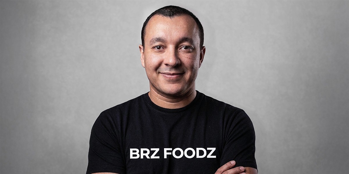 Ricardo Rosa wearing a black BRZ Foodz shirt with his arms crossed against a gray background.