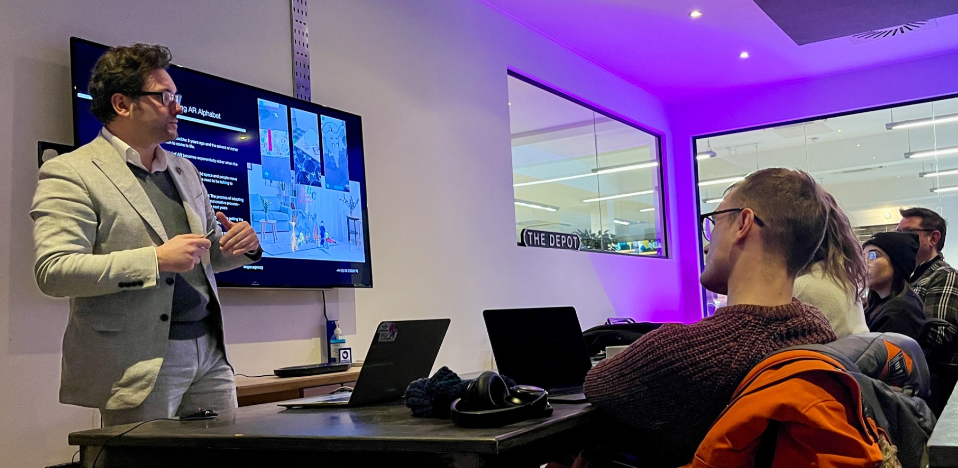 People looking at a tablet and screen with people in the background.