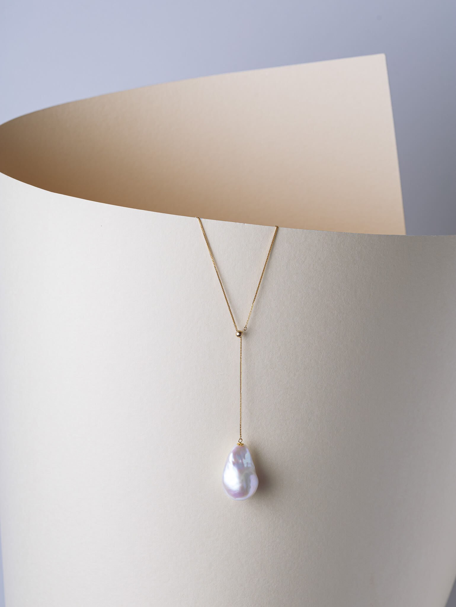 Minimal jewellery still life featuring pearl pendant necklace with curved paper backdrop.