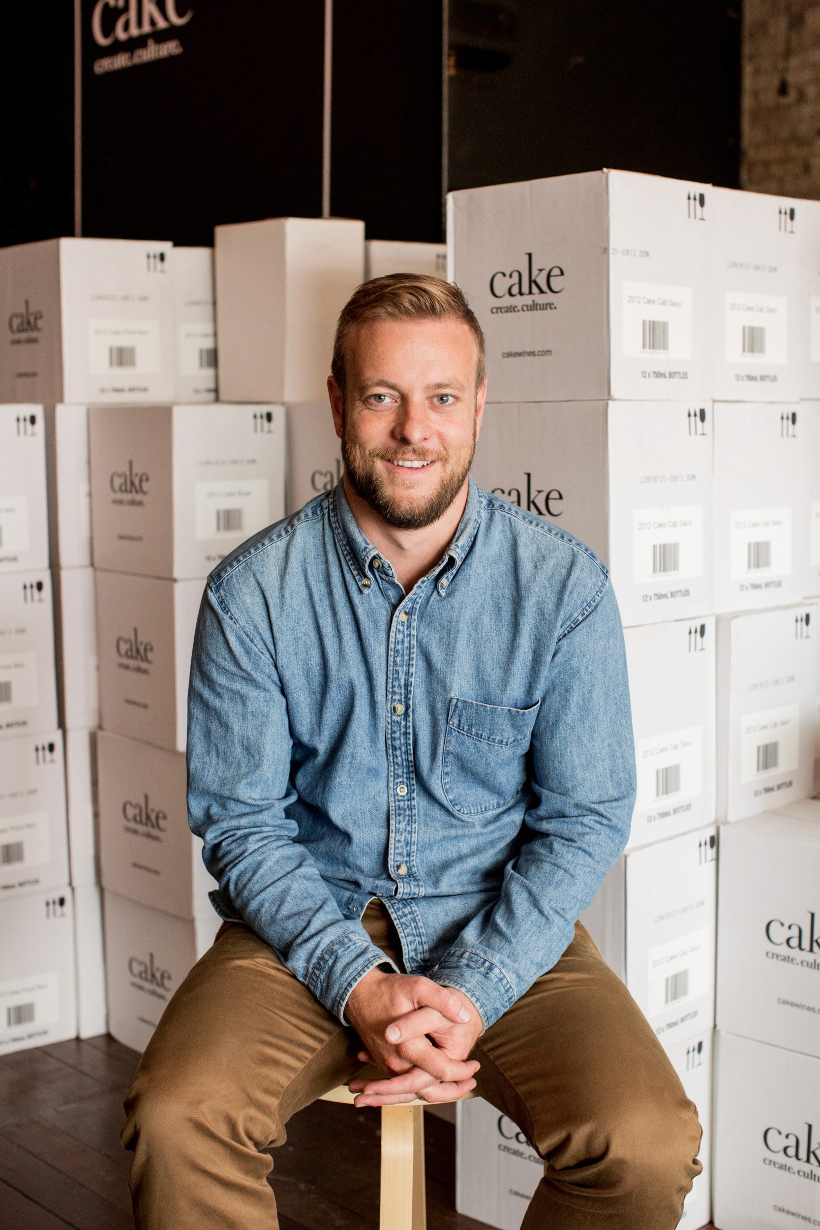 Editorial corporate portrait in Sydney by photographer Cybele Malinowski, featuring a relaxed young man in a black button-down shirt sitting on a rattan chair.