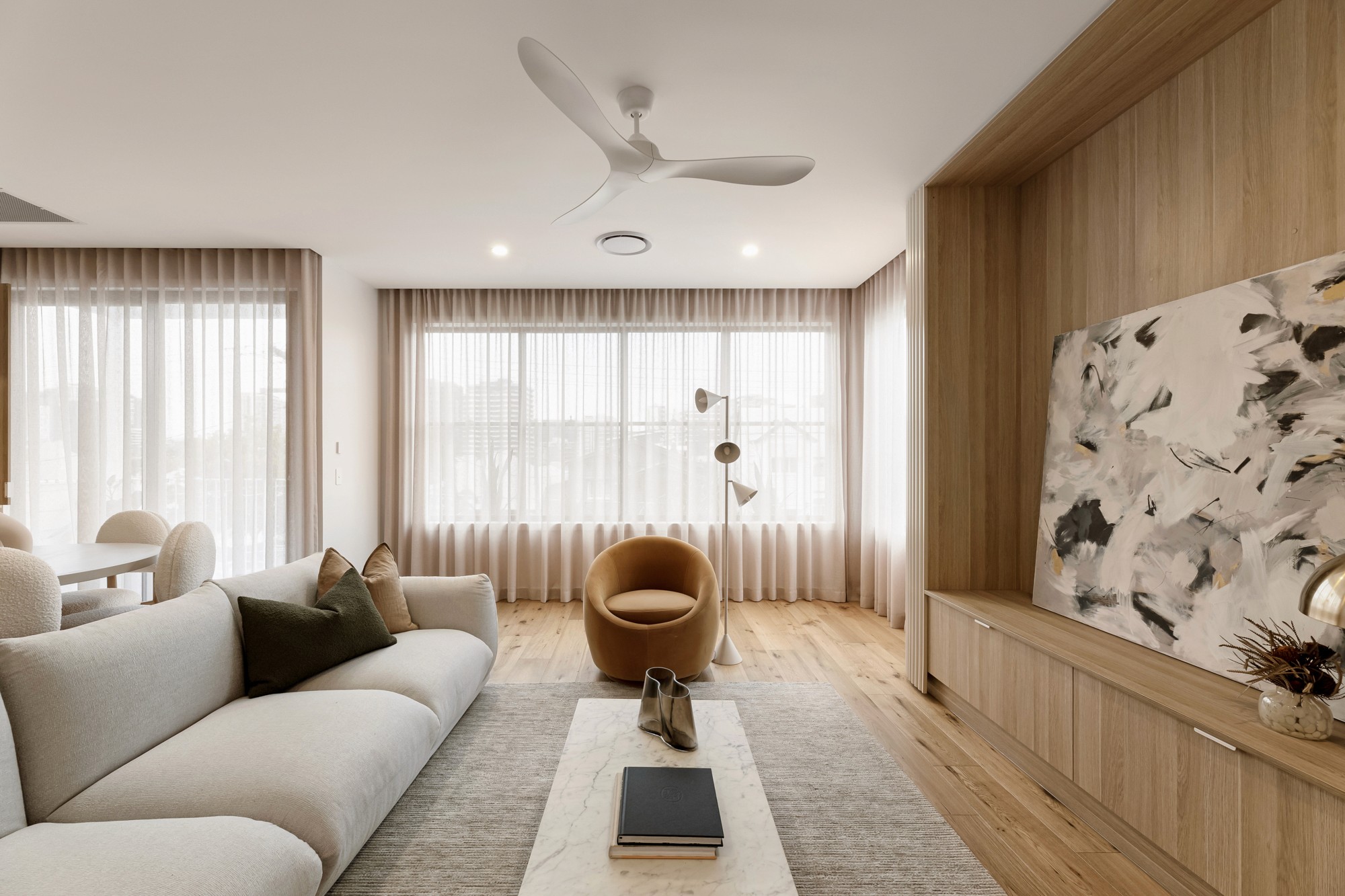 Living room with curved accent chairs, a marble coffee table and custom timber shelving.