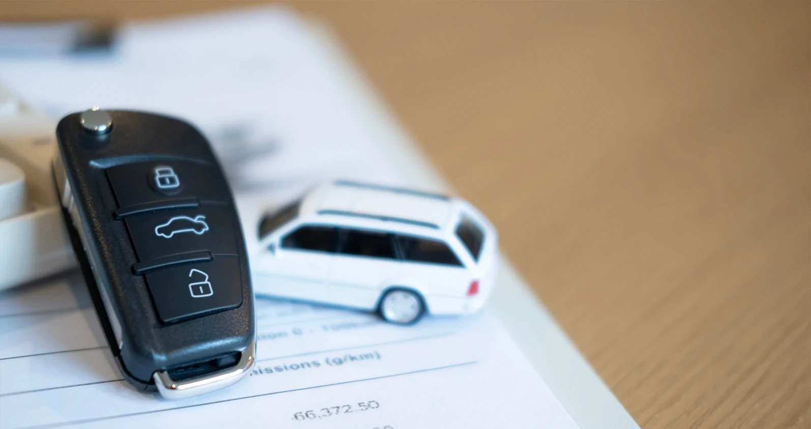 Black car remote or car key and white toy car on financial document, representing cost calculation, auto loan, and car purchase agreement.