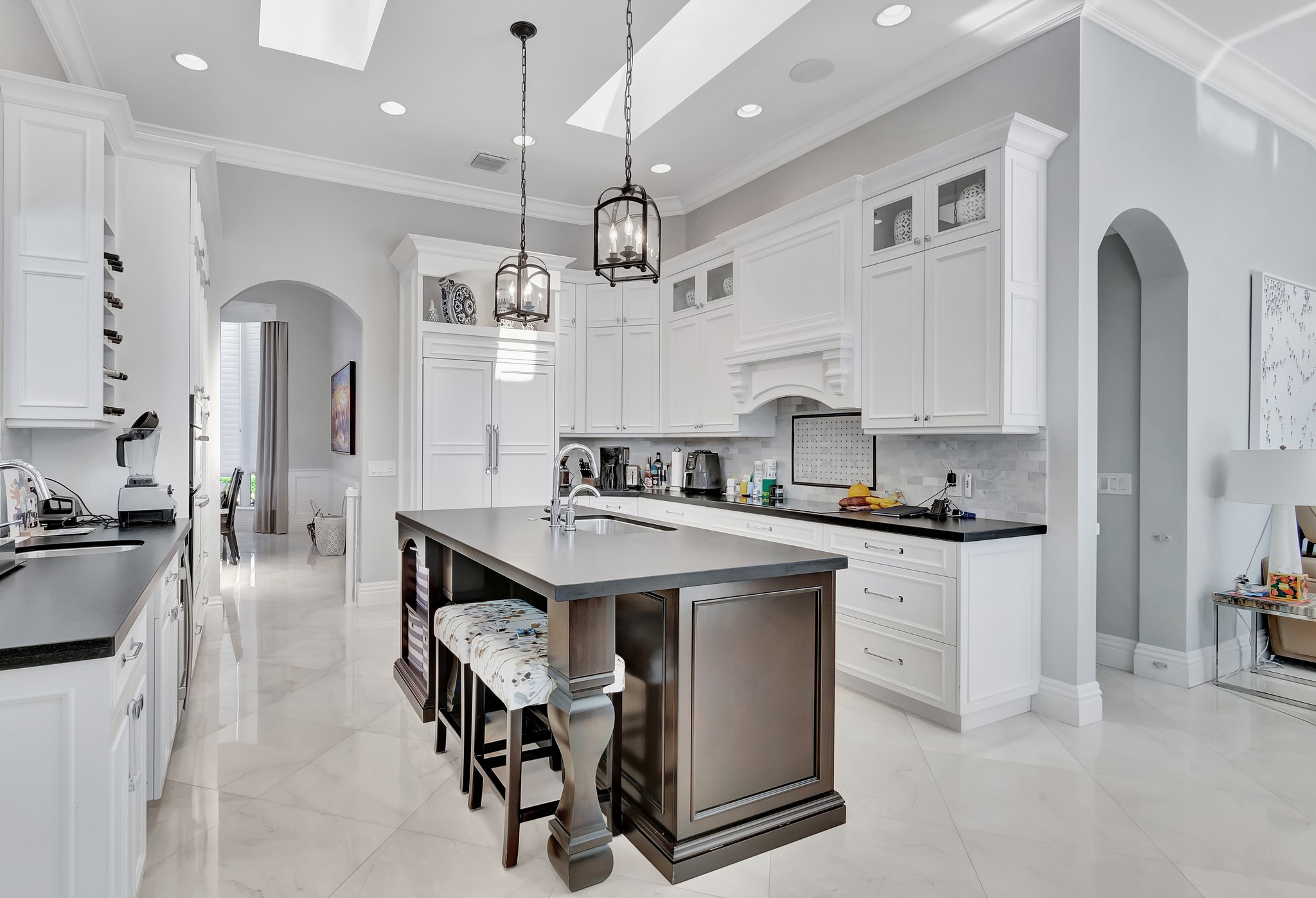 Open concept coastal kitchen with white cabinetry, large center island with wine fridge, pendant lighting, blue patterned rugs, and adjoining living area with blue accent curtains