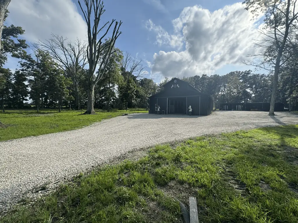 Curved gravel driveway leading to a dark barn among trees
