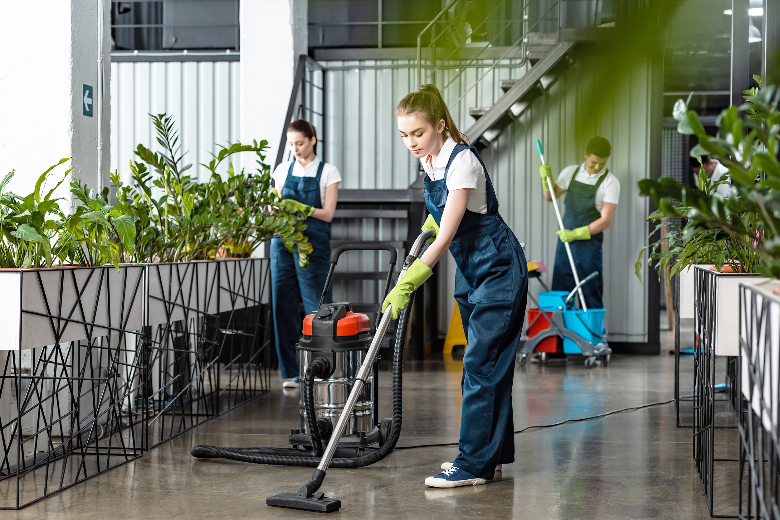 young cleaner vacuuming floor in office near colleagues