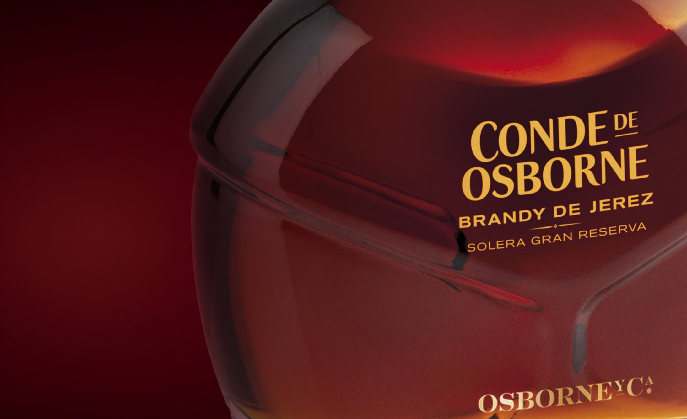 Close-up of a sleek, dark brandy bottle with golden text "Conde de Osborne, Brandy de Jerez, Solera Gran Reserva" against a rich, deep red background.