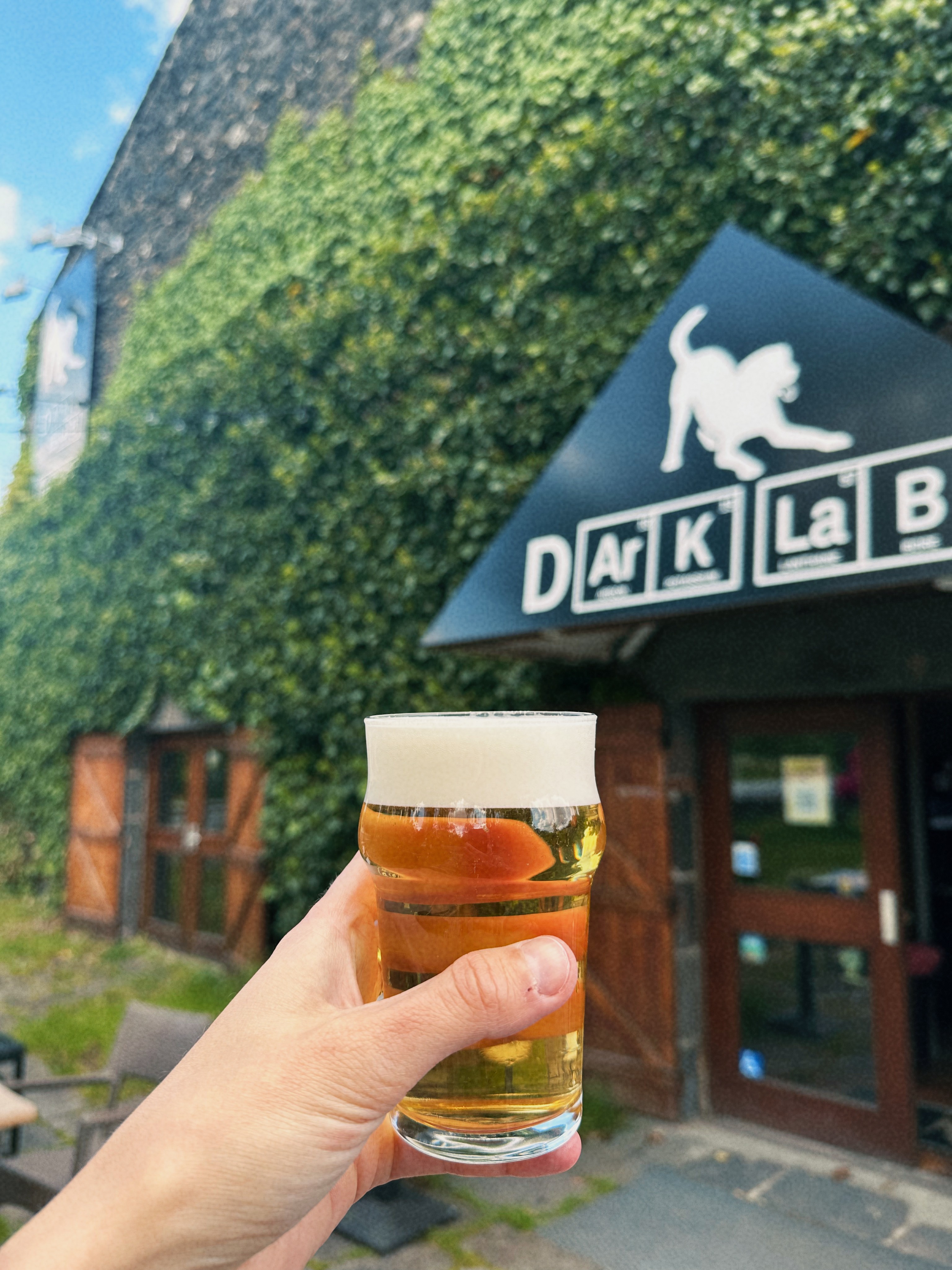 Main qui tient un verre de bière artisanale devant la porte d'entrée Dark Lab