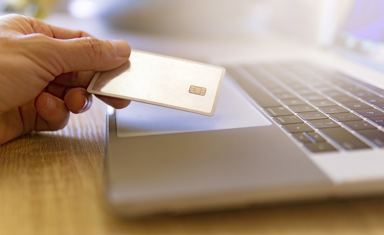 Someone holding a credit card above a laptop