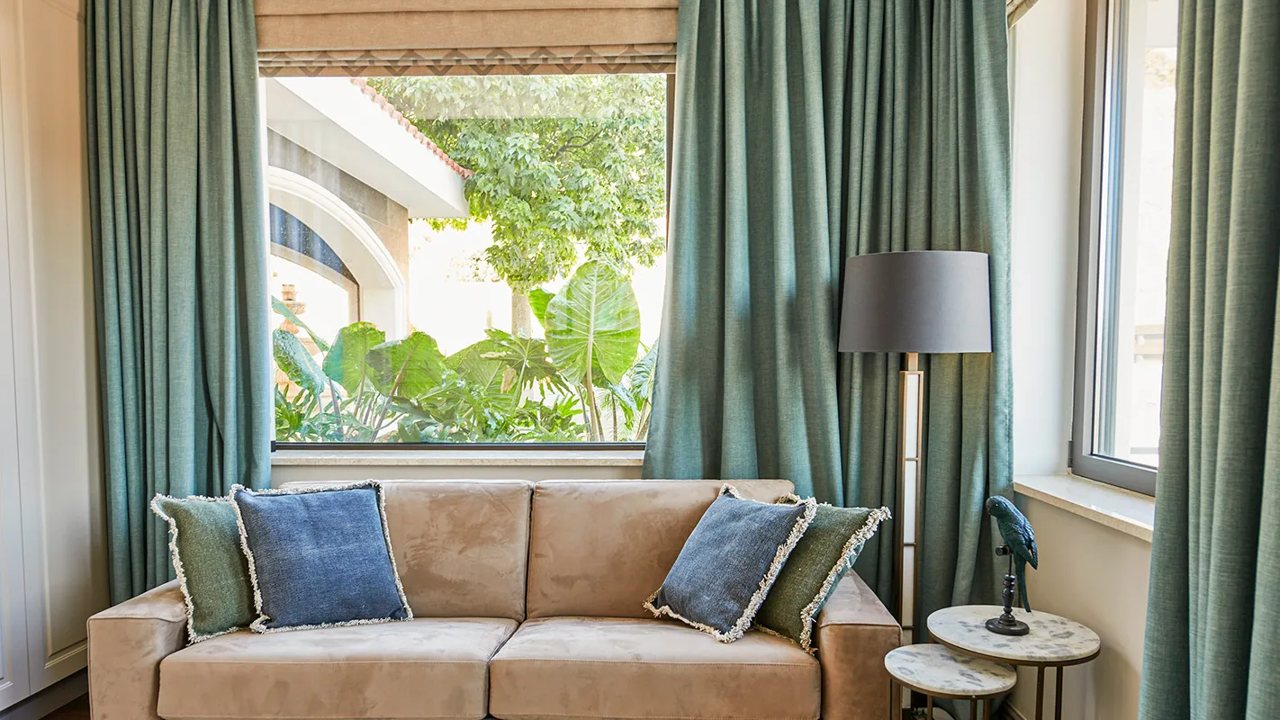 Villa Belmare lounge corner with beige sofa, deep green curtains, and garden-view window seat
