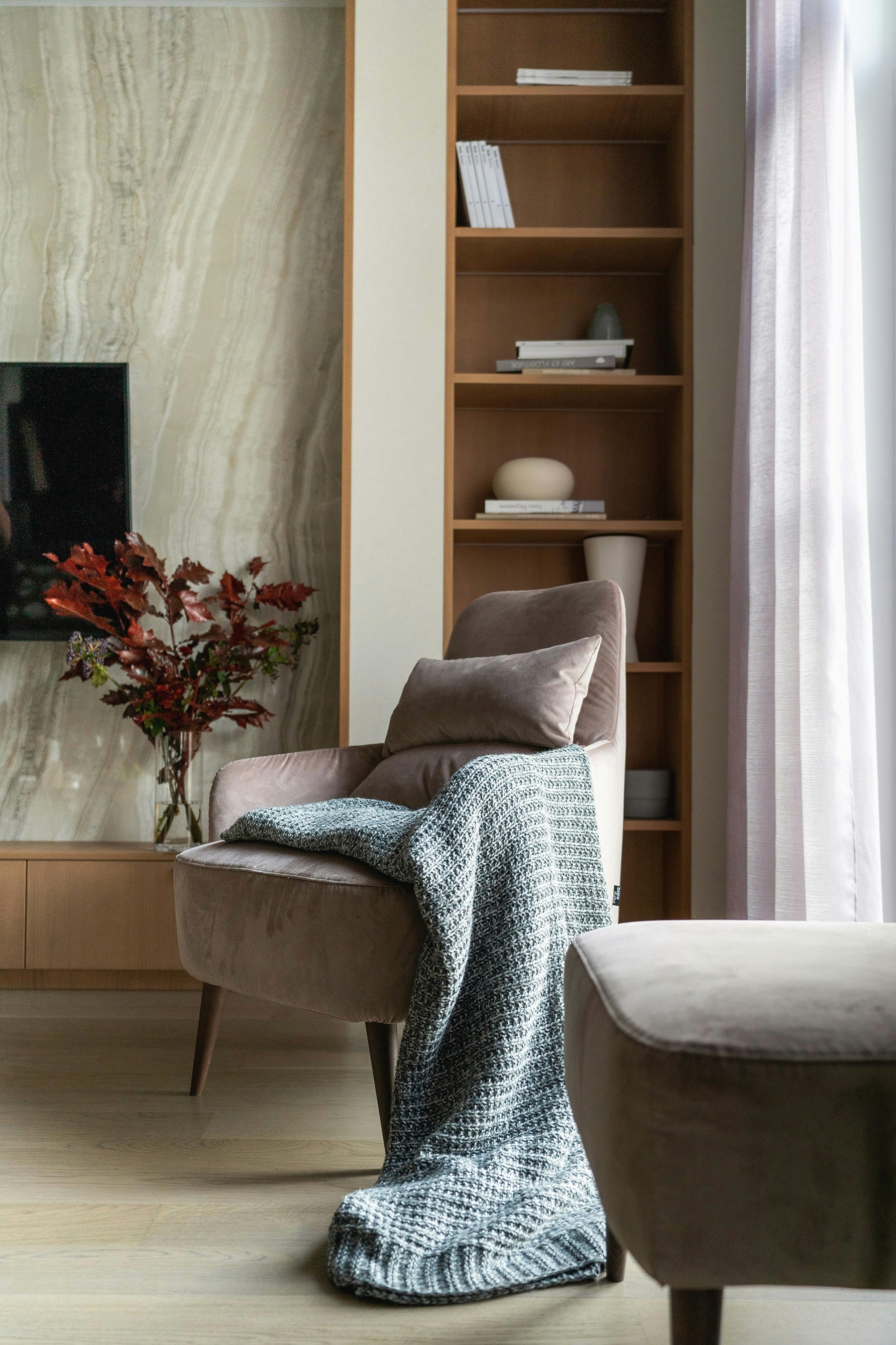 Stylish living room corner with a comfortable chair, knitted blanket, and wooden shelves with decor items