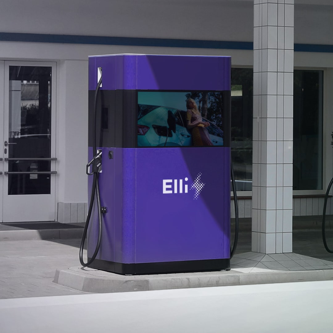 Elli-branded public EV charging unit with dual connectors and a digital display screen, photographed at a forecourt location.