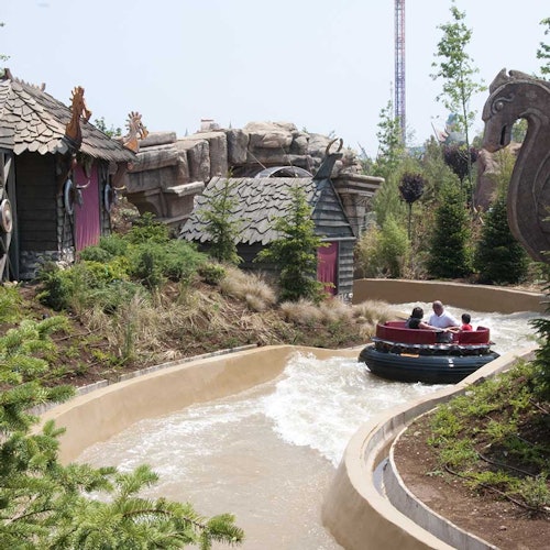 Ihmiset ovat lautalla, joka kulkee mutkittelevan vesireitin läpi, jota ympäröivät vehreä kasvillisuus, maalaismaiset rakennukset ja kivirakennelmat.