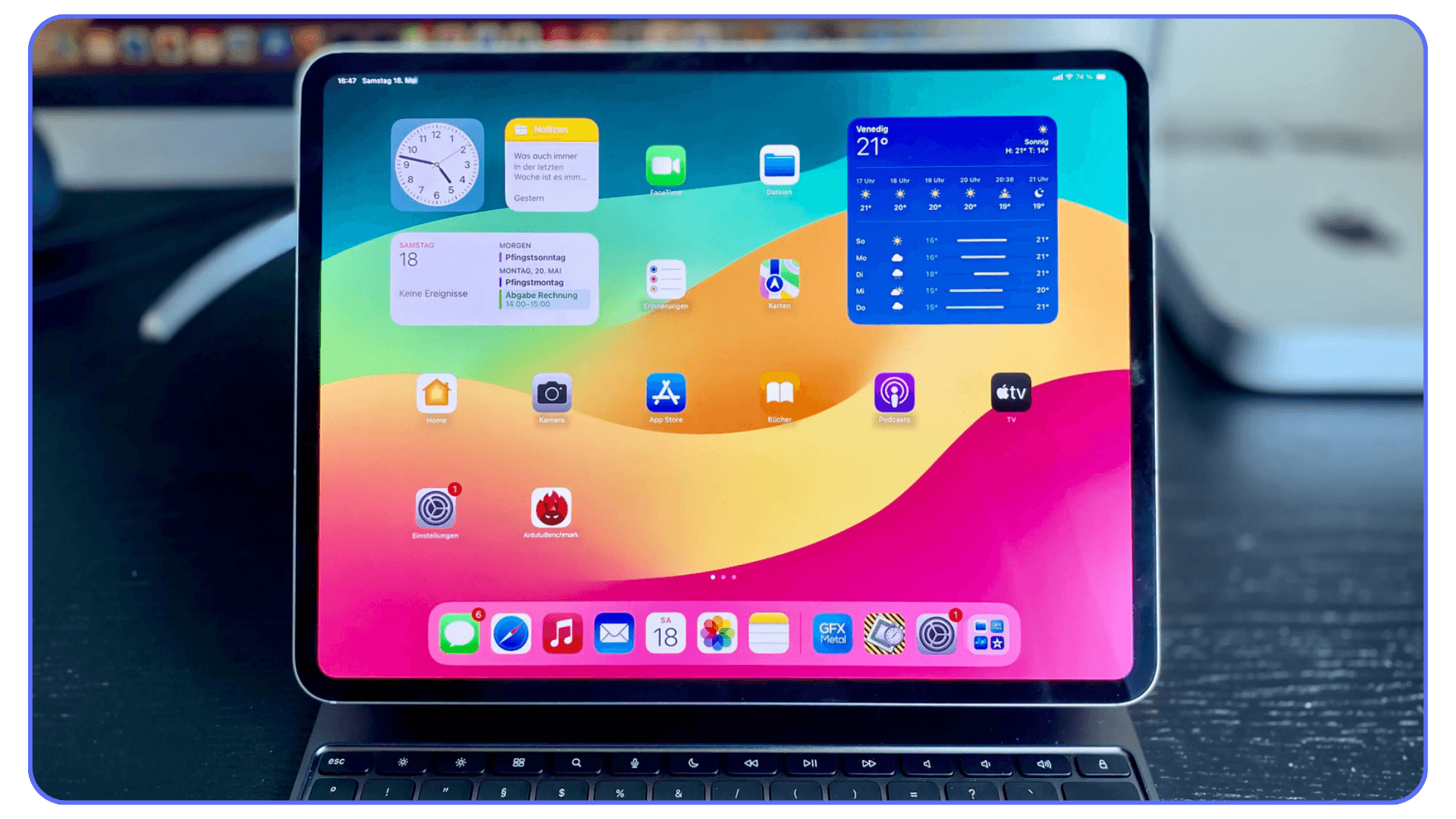 iPad on a keyboard stand showing home screen with clock, notes, and weather widgets, along with various app icons on a colorful background.