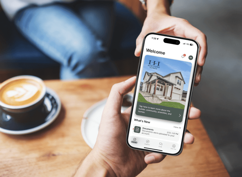 Hands holding a phone showing a home builder app welcome screen beside a coffee