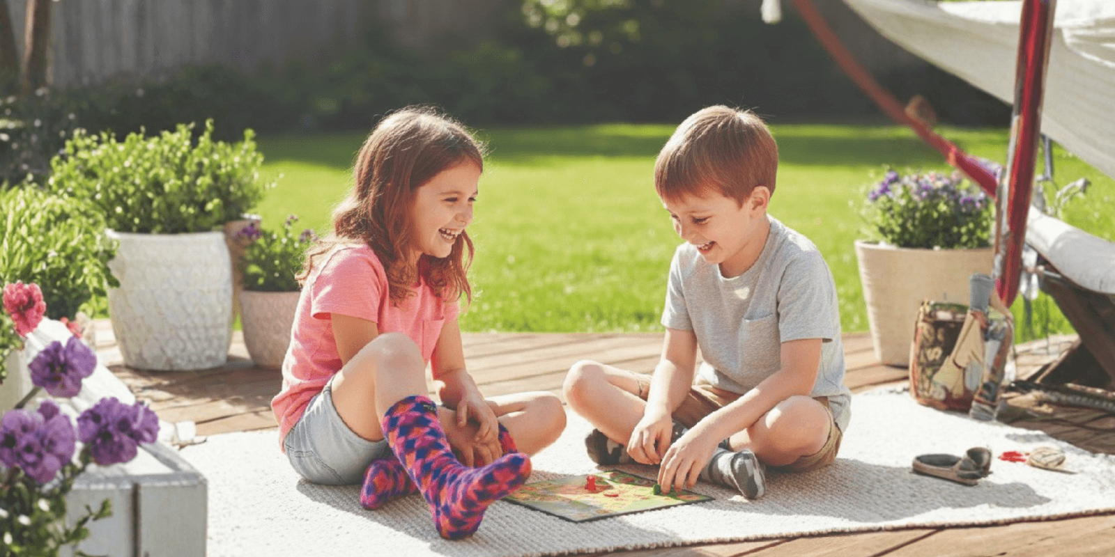 The image features two children joyfully playing a board game outdoors, symbolizing the warmth, comfort, and inclusivity of Polar Feet products.
