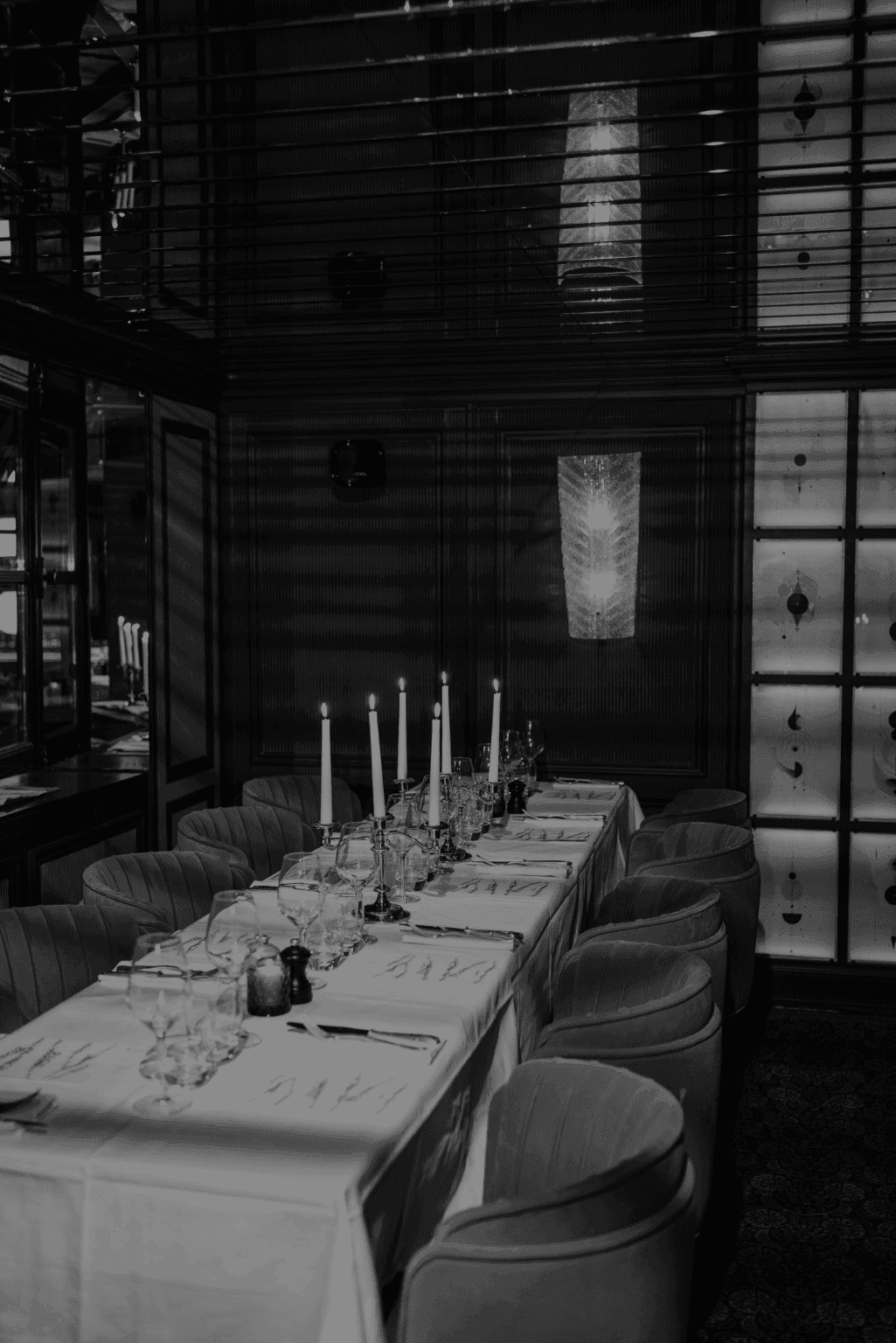 A dimly lit, elegant dining room set with tall candles, crystal glasses, and plush velvet chairs — exuding intimacy, sophistication, and timeless charm.  