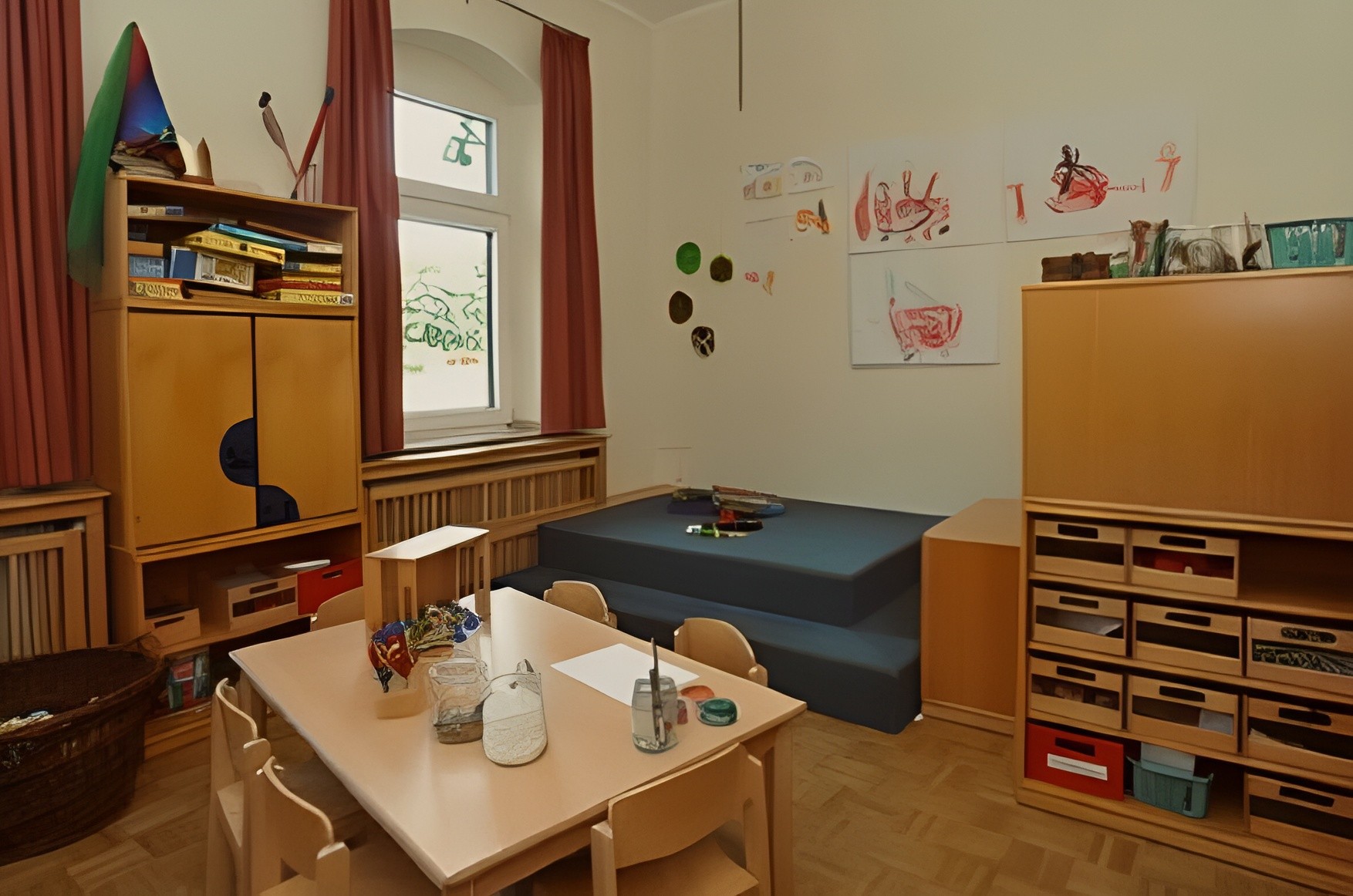 Ein gemütlicher, gut beleuchteter Kindergarten-Raum mit einem kleinen Tisch, Stühlen, Regalen und buntem Dekor an den Wänden.