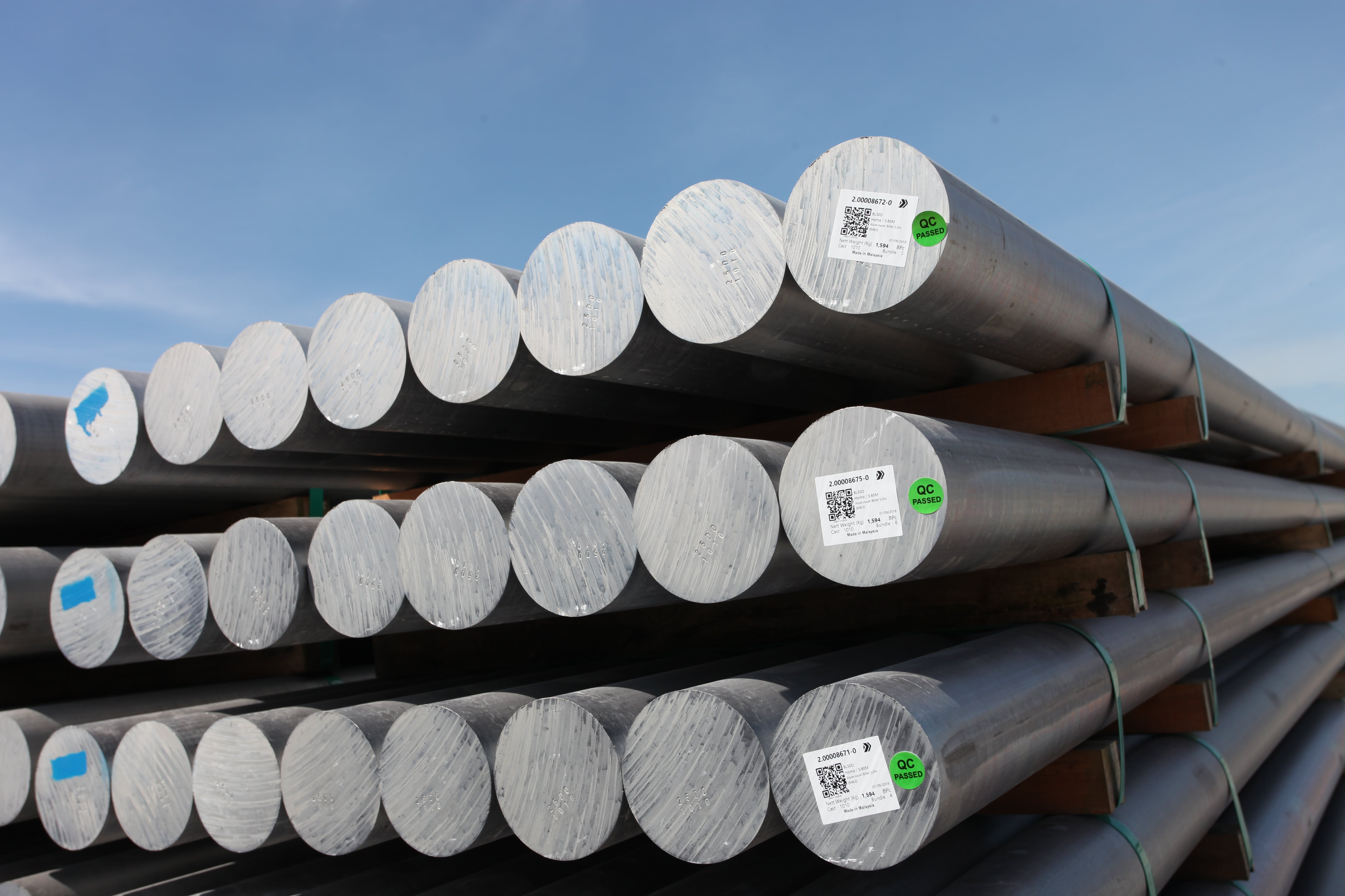 Stacked aluminum round bars with labels against a blue sky.