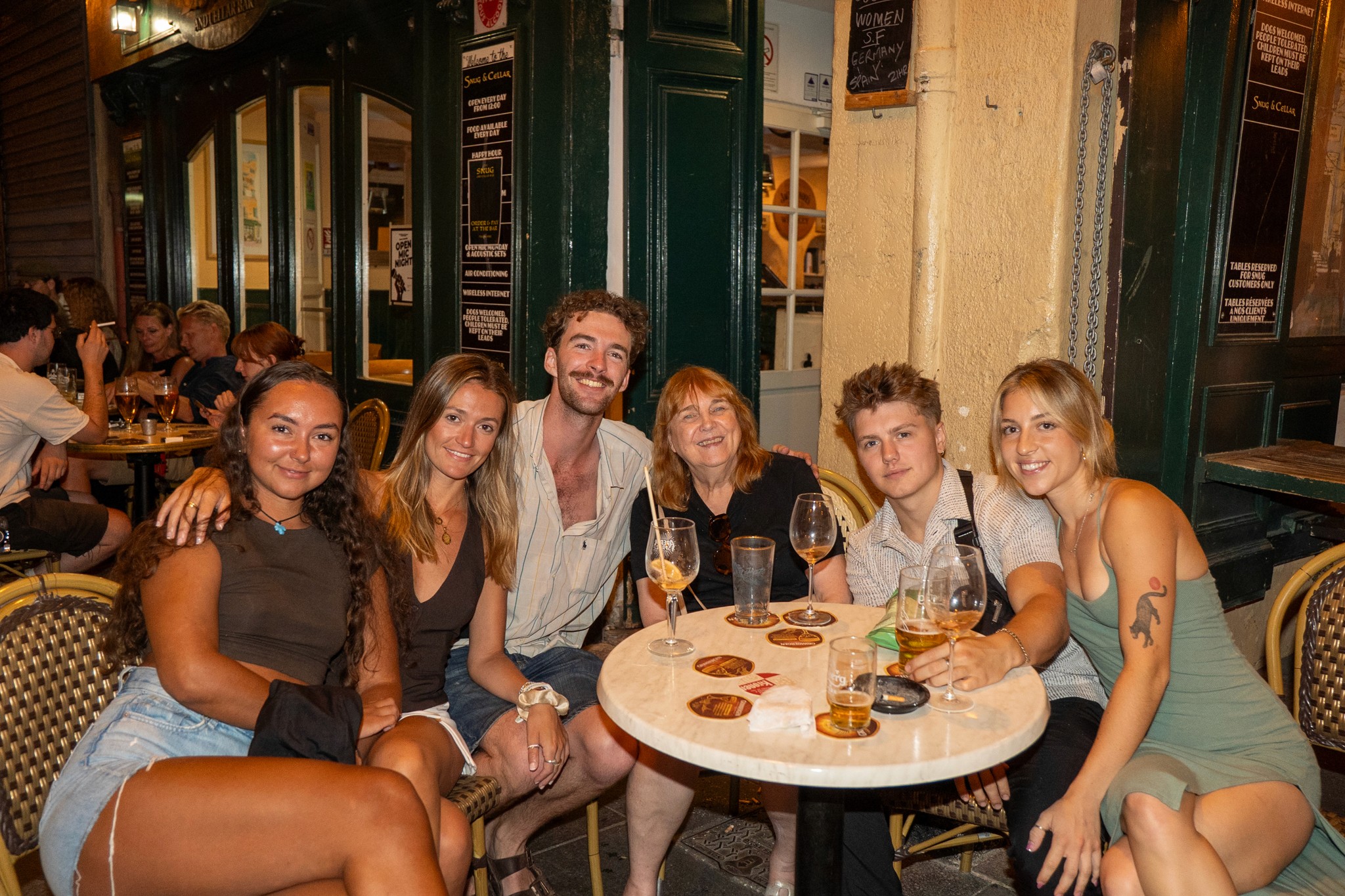 A group of international travelers walking together at night through a European city center, laughing and heading toward lively bars.