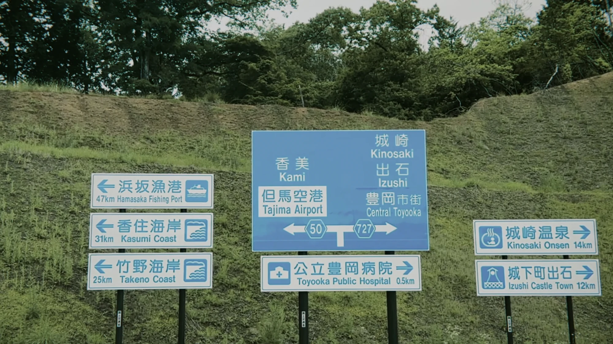 Blue Japanese road sign pointing to Kinosaki Onsen, Izushi, Tajima Airport and the Takeno coast.