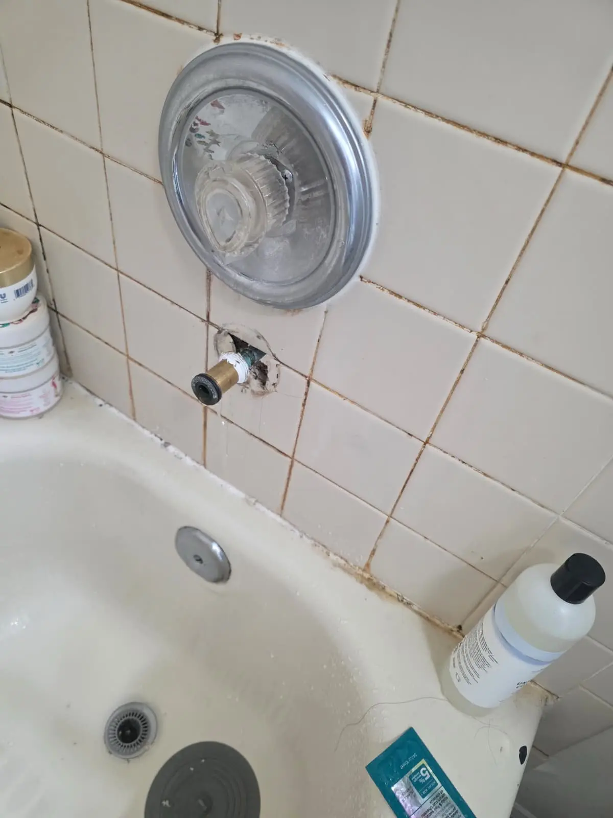 A bathtub tile wall with an exposed tub spout pipe dripping water, undergoing a targeted shower repair.