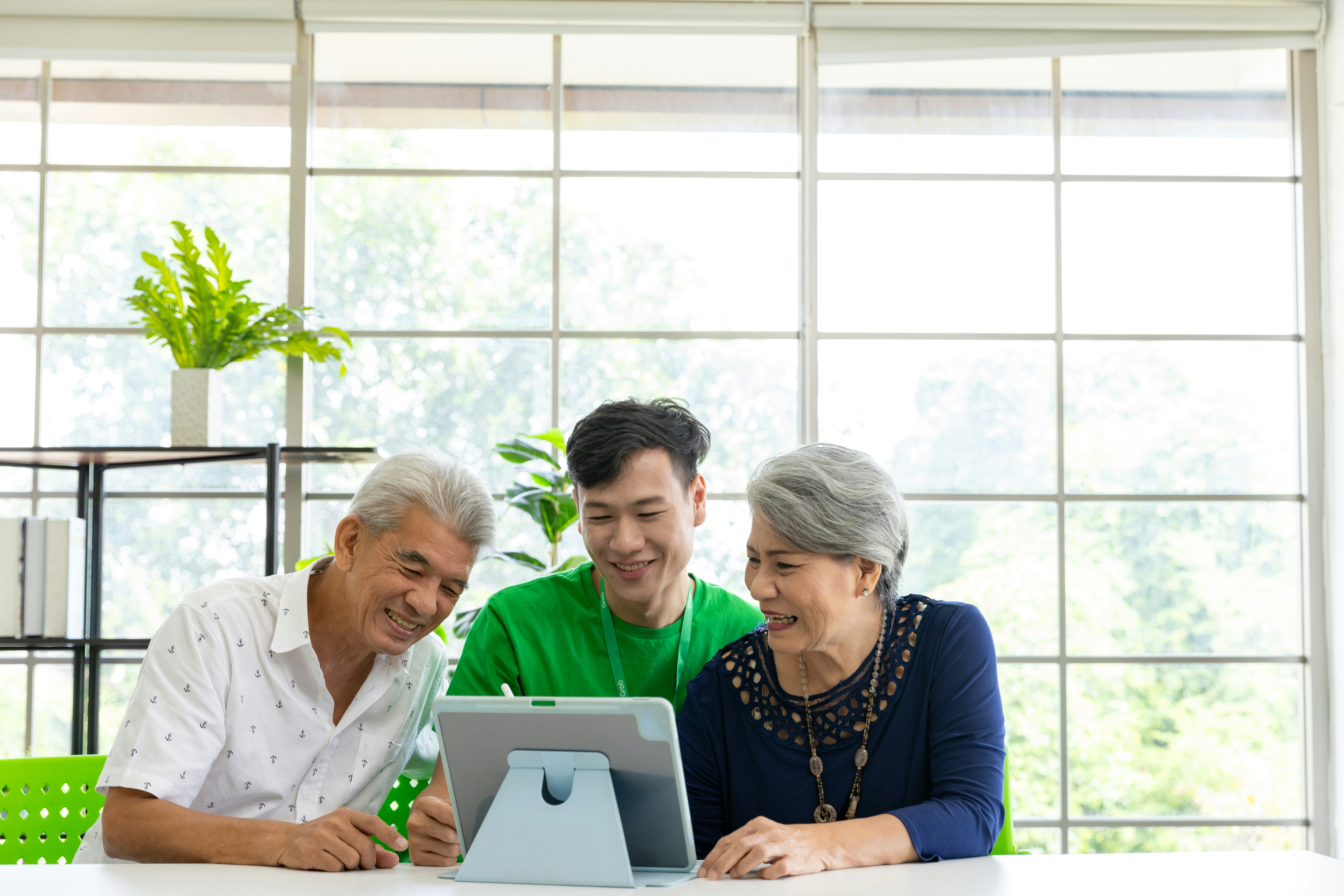 Photo of 3 people, seated, smiling and operating an ipad propped up on a table