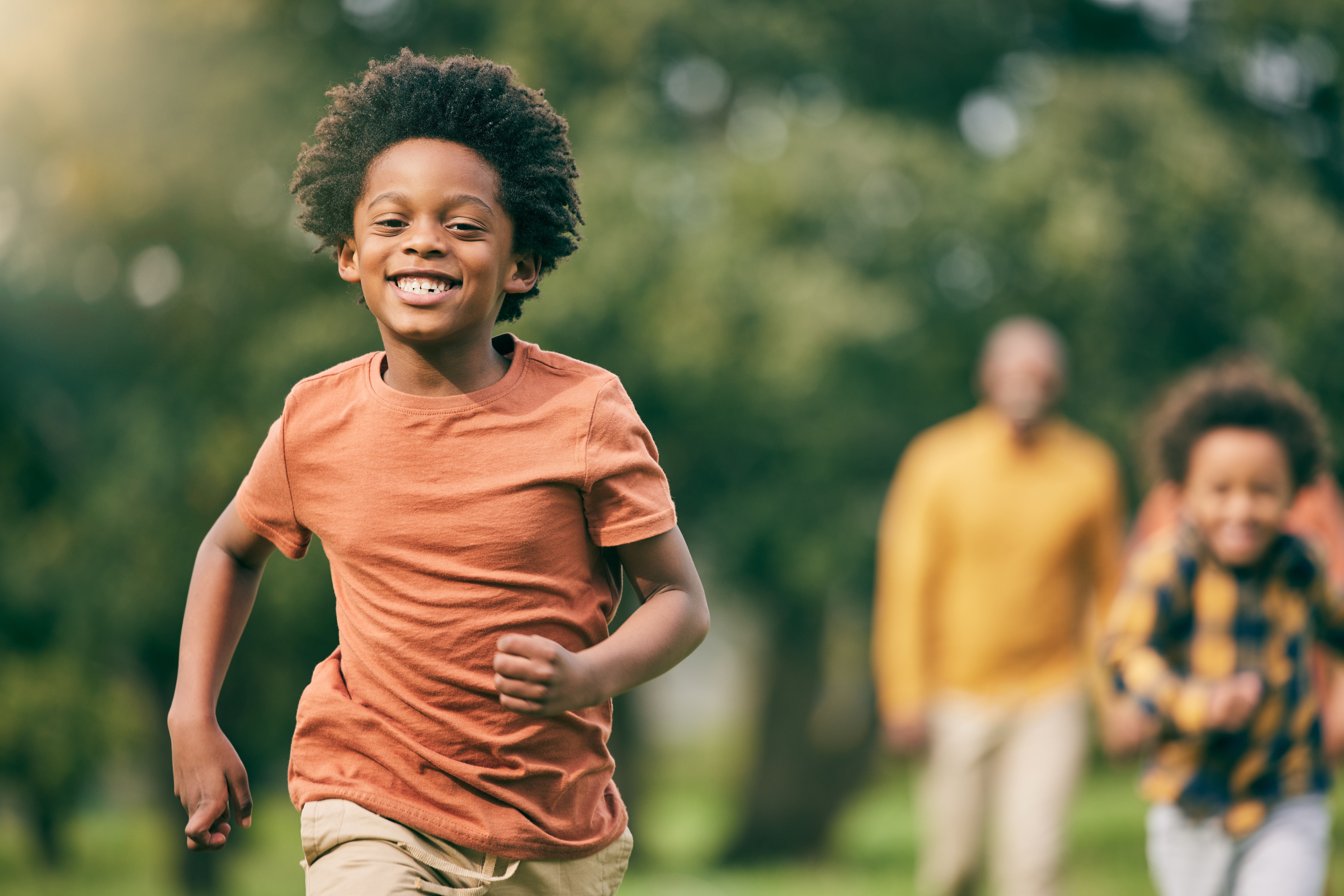 Boy in an orange t-shirt running happily through a park