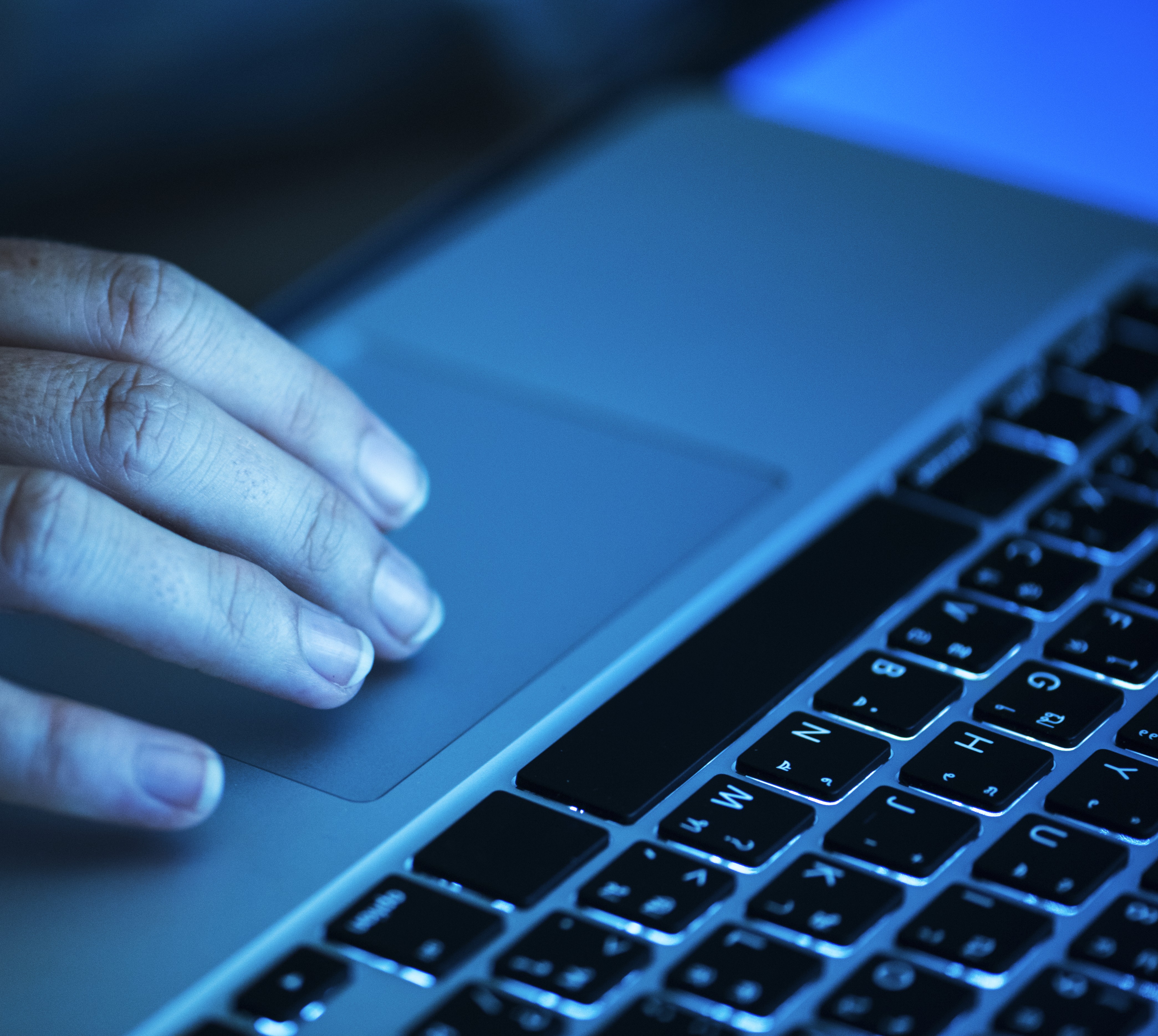 A talent recruiter with a soft smile working on her laptop in the office. The angle is on her face so we can't see what's is on the screen. She is wearing a blazer