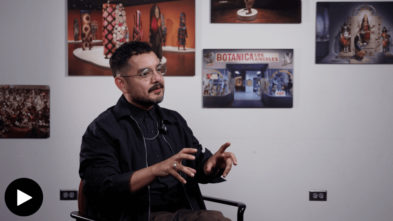 Andres Estrada, seated, speaking with unframed images behind him